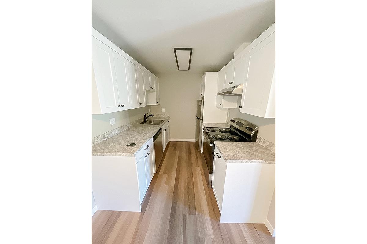 Modern kitchen featuring white cabinetry, granite countertops, and stainless steel appliances. The layout includes a stove, oven, and sink along with ample counter space. The flooring is a light wood look, creating a bright and inviting atmosphere.