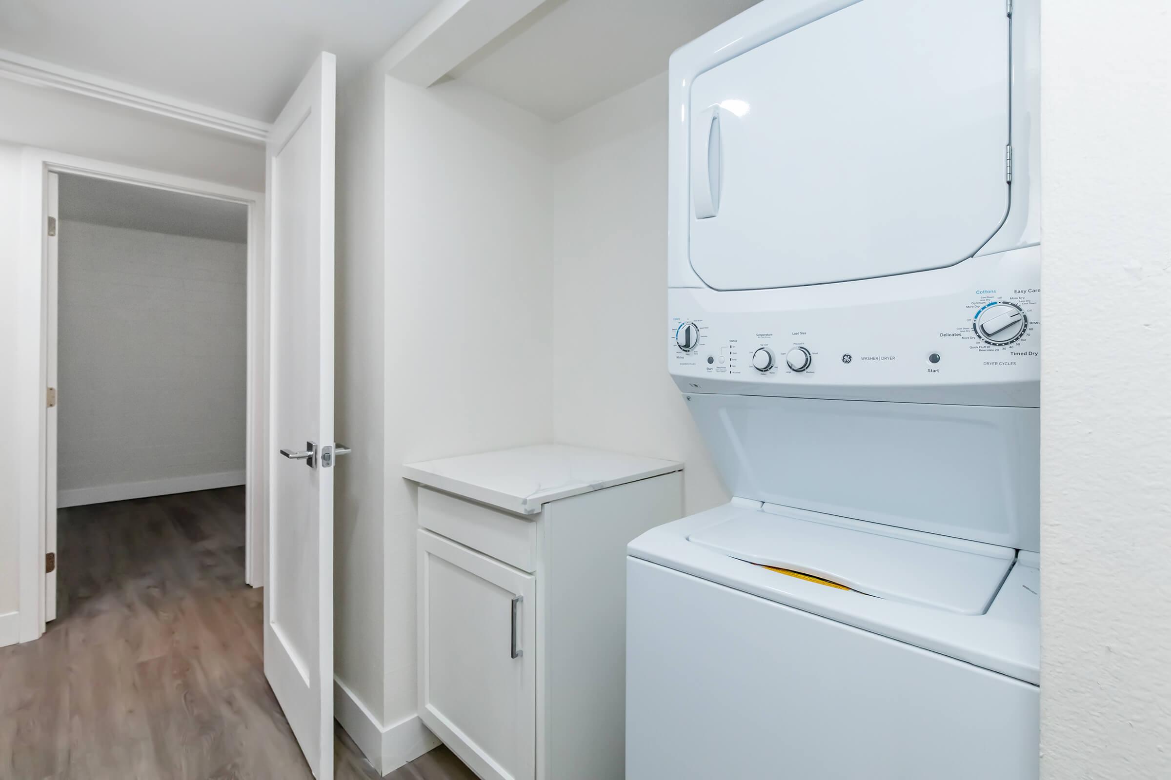 A compact laundry area featuring a stacked washer and dryer unit, alongside a countertop for folding clothes. The space is well-lit with neutral-colored walls and a door leading to an adjacent room, showcasing modern design and functionality.
