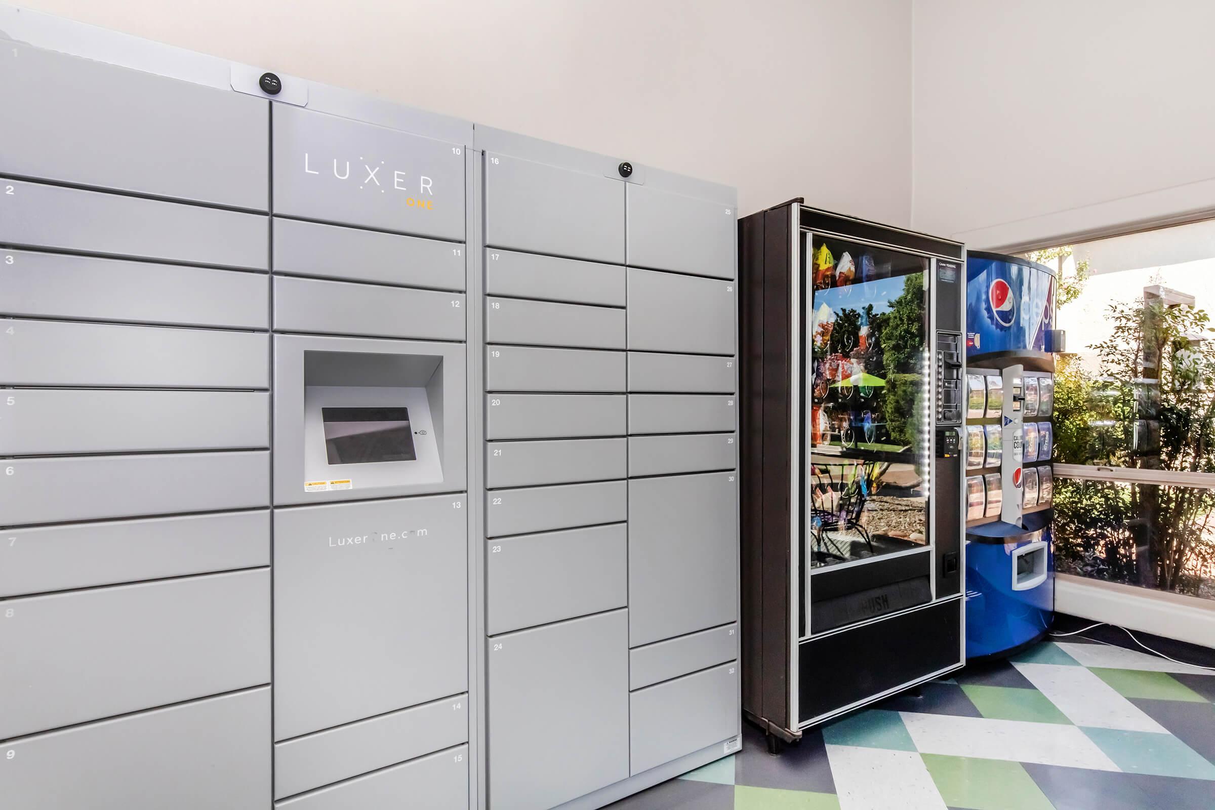 A modern package delivery locker system labeled "LUXER" stands adjacent to a vending machine displaying Pepsi products. The interior features bright, geometric floor patterns and large windows allowing natural light.