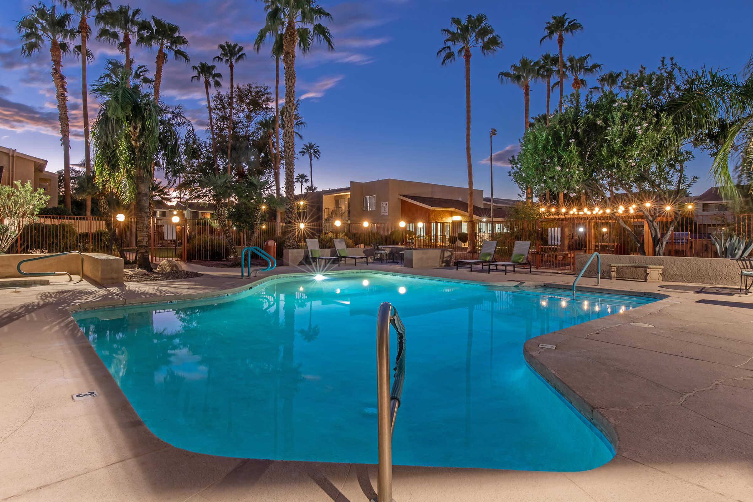 A serene swimming pool surrounded by palm trees and lounge chairs, with a warm evening glow from string lights. The sky is transitioning to dusk, and the atmosphere is calm and inviting, perfect for relaxation.