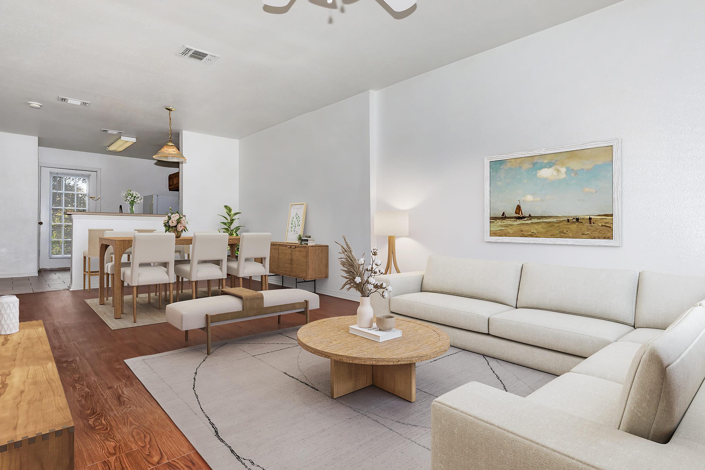 A modern and bright living room featuring a light-colored sofa and a round coffee table. The space includes a dining area with beige chairs and a wooden table. A large painting is hung on the wall, and a light fixture decorates the ceiling. Plants add a touch of greenery to the inviting atmosphere.