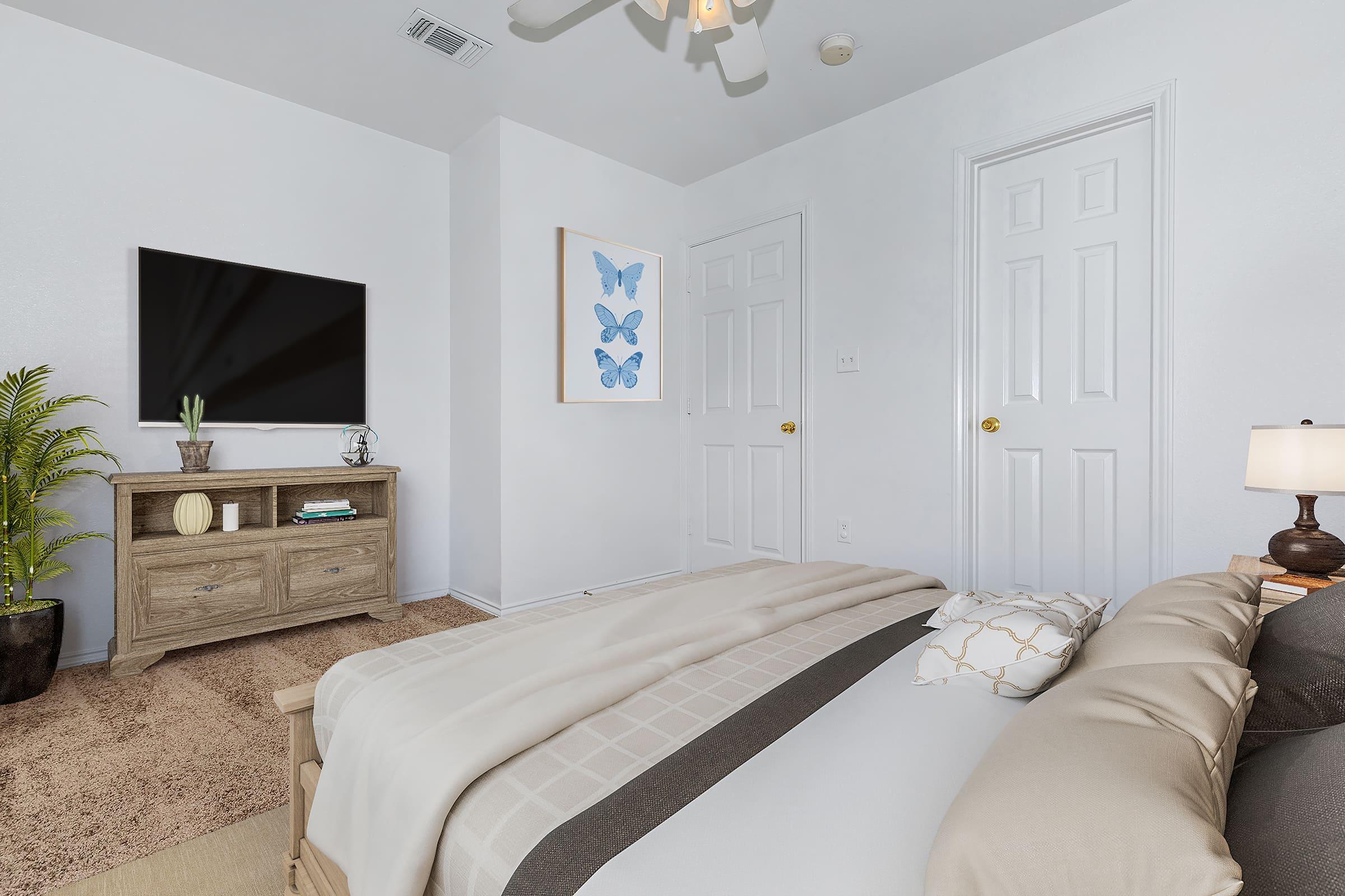 A cozy bedroom featuring a large bed with neutral bedding, a decorative pillow, and a bedside lamp. A wooden dresser stands against the wall with a flat-screen TV mounted above it. A piece of butterfly art hangs on the wall, and a potted plant adds a touch of greenery to the space. Two white doors are visible.