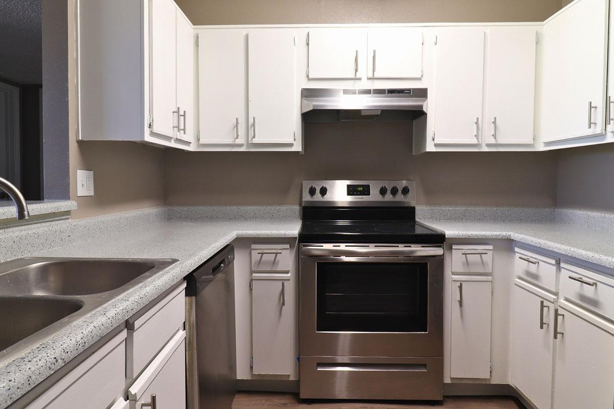 A modern kitchen featuring white cabinets, a stainless steel oven and microwave, a double sink, and a dishwasher. The countertop is light-colored and the walls are painted a neutral shade, creating a clean and spacious appearance.