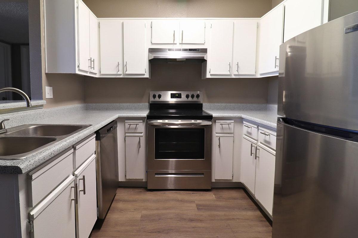 Modern kitchen featuring white cabinetry, a stainless steel oven and refrigerator, and a gray countertop. There are dual sinks and a dishwasher, with laminate flooring visible. The space is well-lit and organized, ideal for cooking and meal preparation.