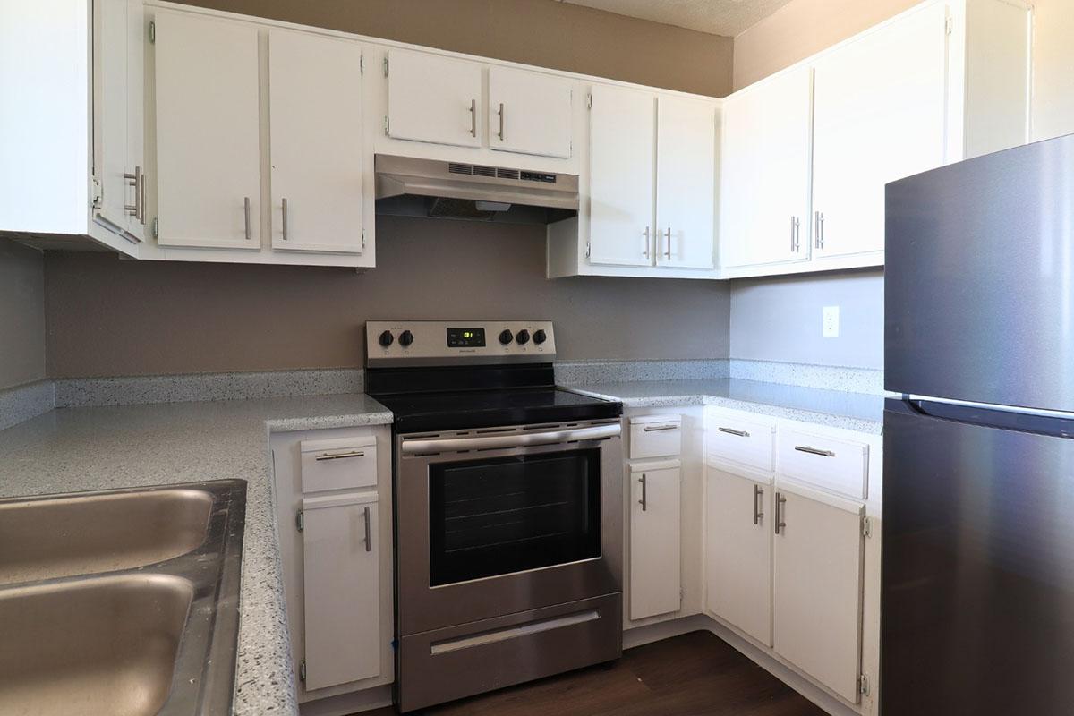 Modern kitchen featuring white cabinets, a stainless steel oven and stovetop, a silver refrigerator, and a double sink. The countertops are made of light-colored granite, and the walls are painted in a neutral tone, creating a clean and contemporary look.