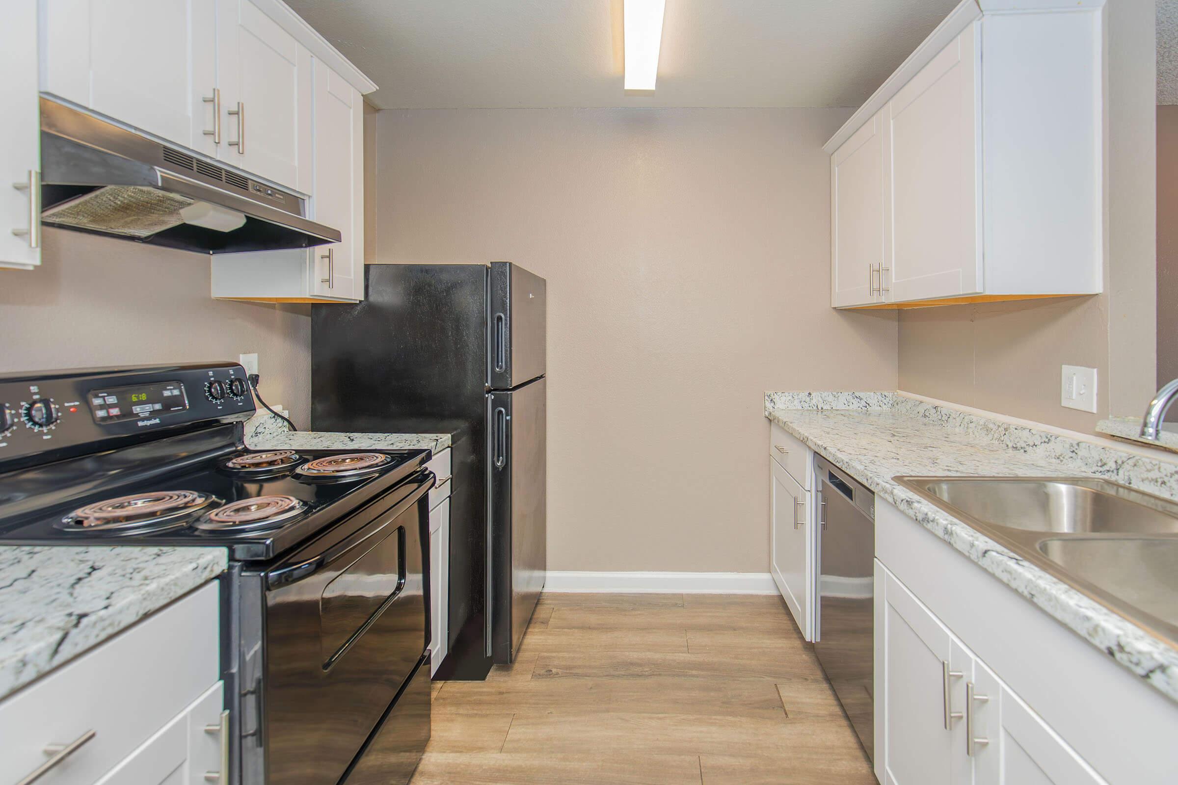 Modern kitchen featuring white cabinetry, a black refrigerator, a stainless steel oven with an electric cooktop, and a double sink. Countertops are made of granite, and the flooring is wood-like. The space is well-lit with overhead lighting, creating a bright and inviting atmosphere.