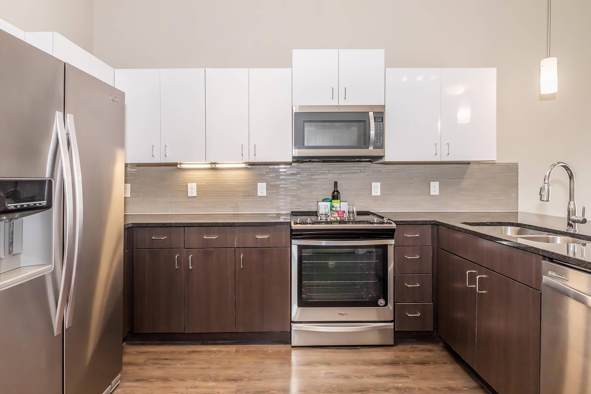 A modern kitchen featuring stainless steel appliances, including a refrigerator and stove. The cabinetry is a mix of dark wood and white, with a sleek countertop. Under-cabinet lighting highlights the space, and a stylish sink is installed next to the stove. The overall design is clean and contemporary.