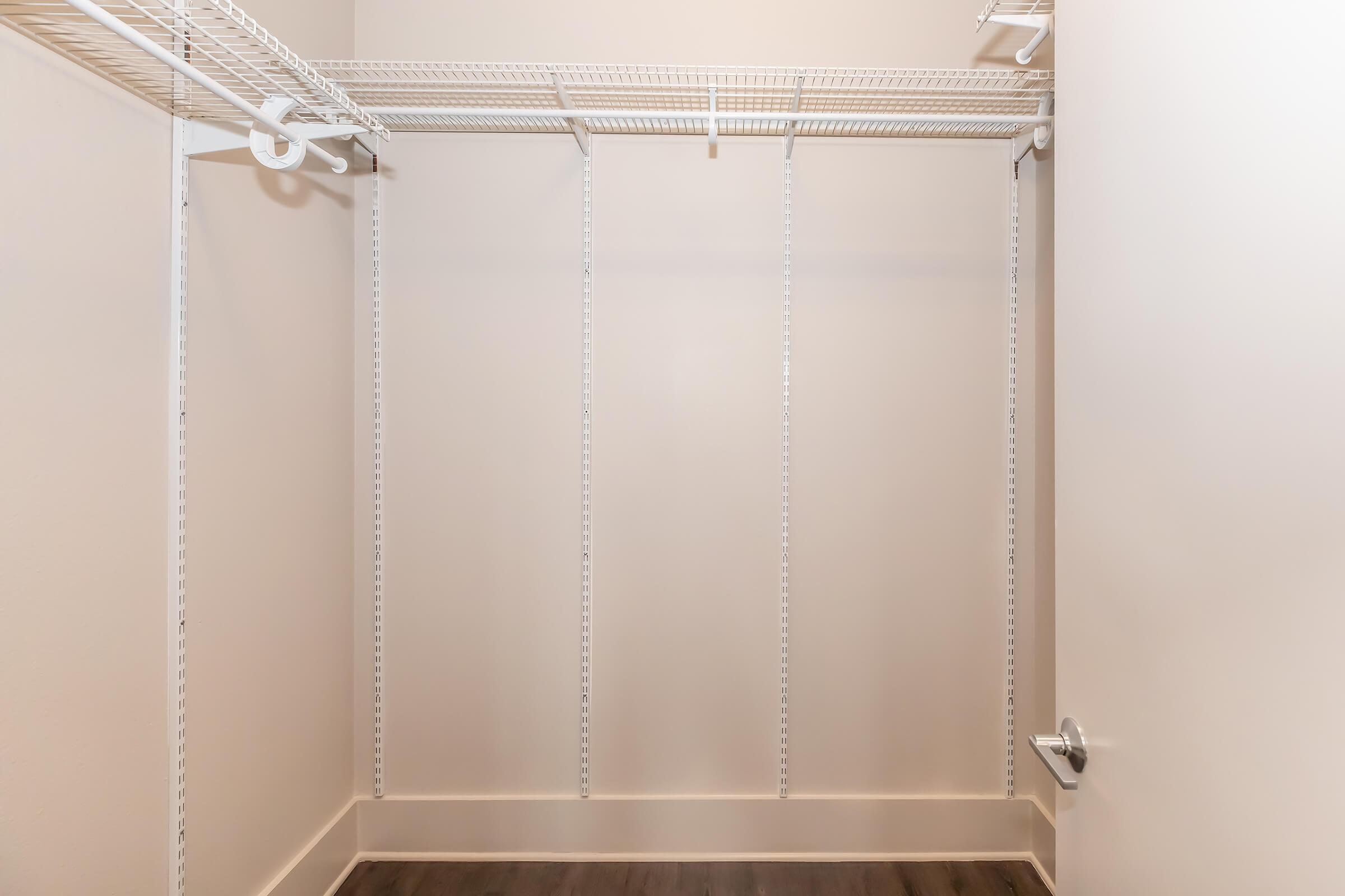 Empty closet with white wire shelving and a light beige wall. The floor is dark wood, and there is a door handle visible on the right side. The space is clean and uncluttered, suitable for storage or organization.
