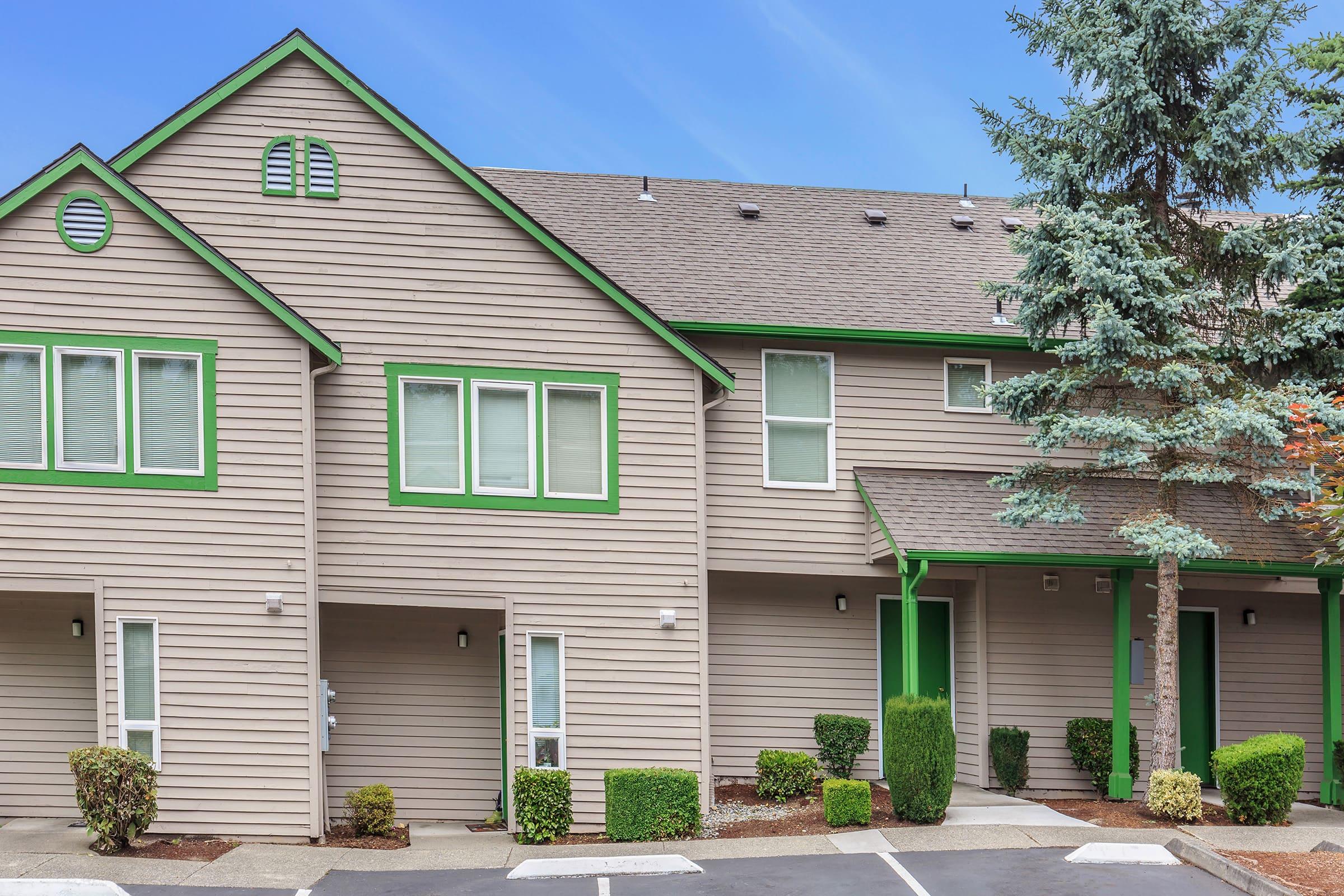 A two-story residential building featuring a light brown wooden exterior with green trim.
