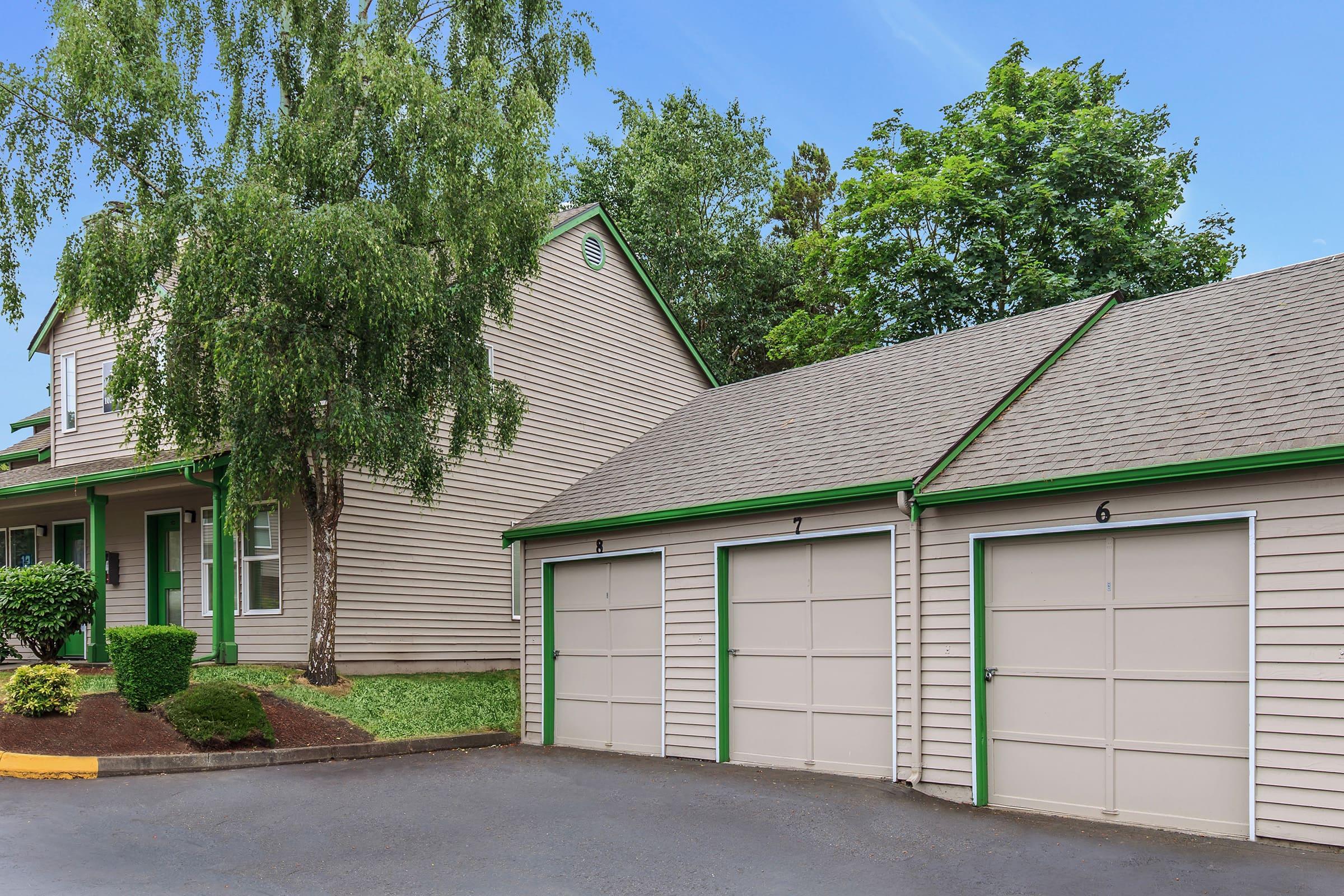 A two-story house with light brown siding and green trim, surrounded by trees.
