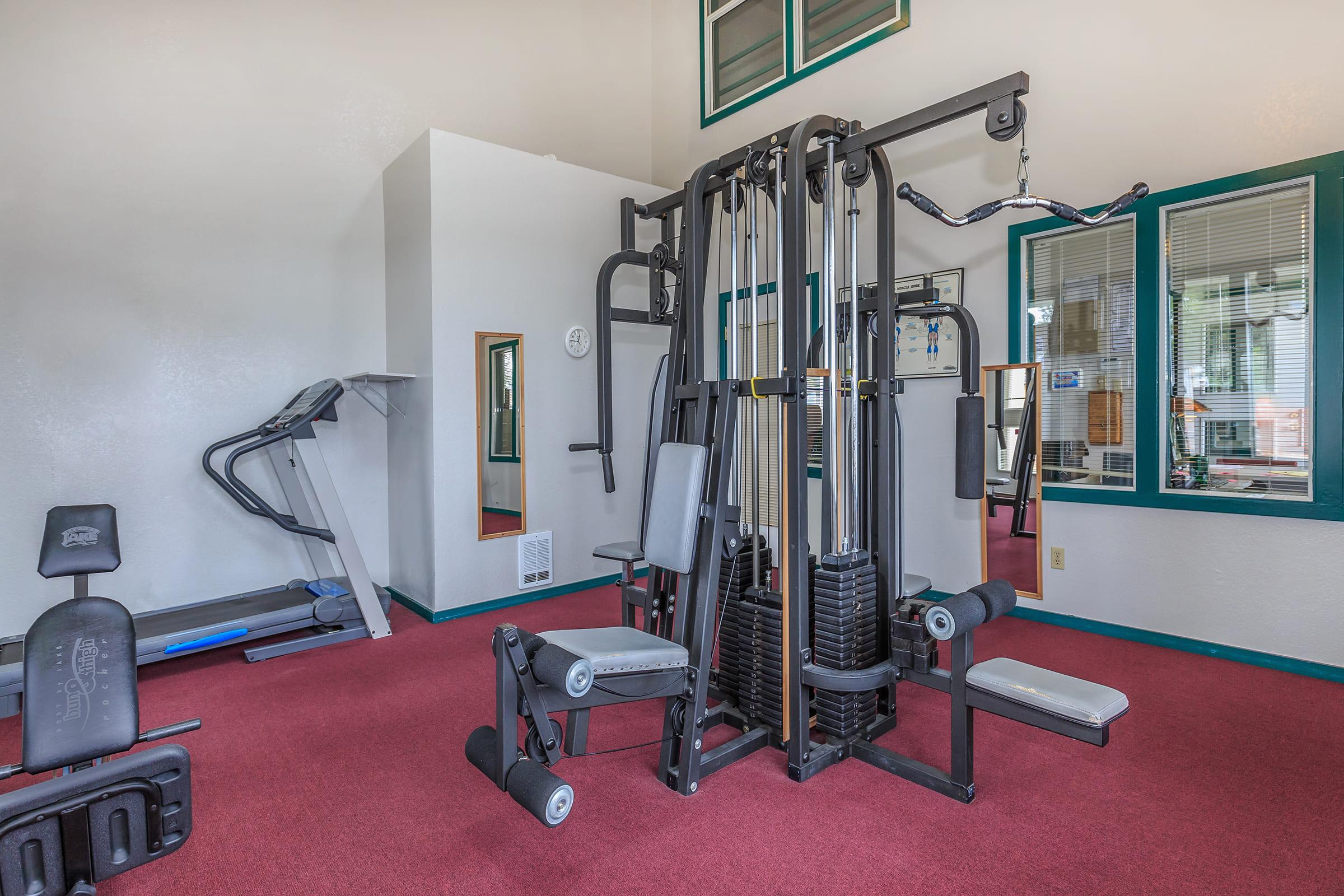 A spacious gym area featuring a multifunctional weight machine, treadmill, and weight bench.