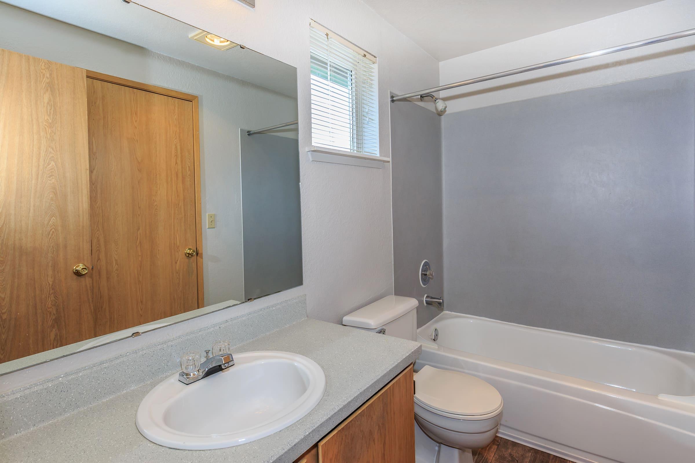 A clean and modern bathroom featuring a white bathtub with a shower curtain, a toilet, and a sink with a countertop.