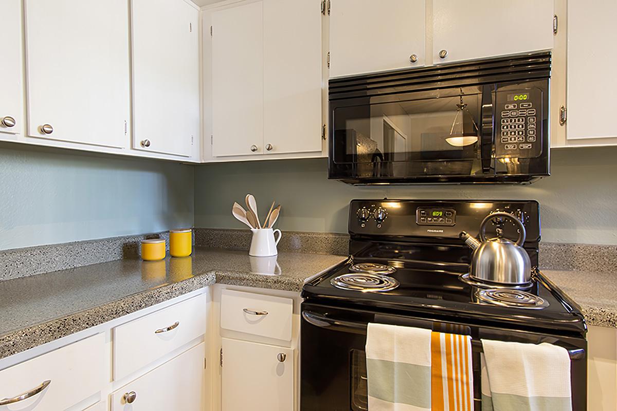 A modern kitchen featuring a black stove with a microwave above, light-colored cabinetry, and a countertop with a kettle and kitchen utensils. There are two yellow canisters and a striped towel draped over the stove. The walls are painted a light blue, creating a fresh and inviting atmosphere.