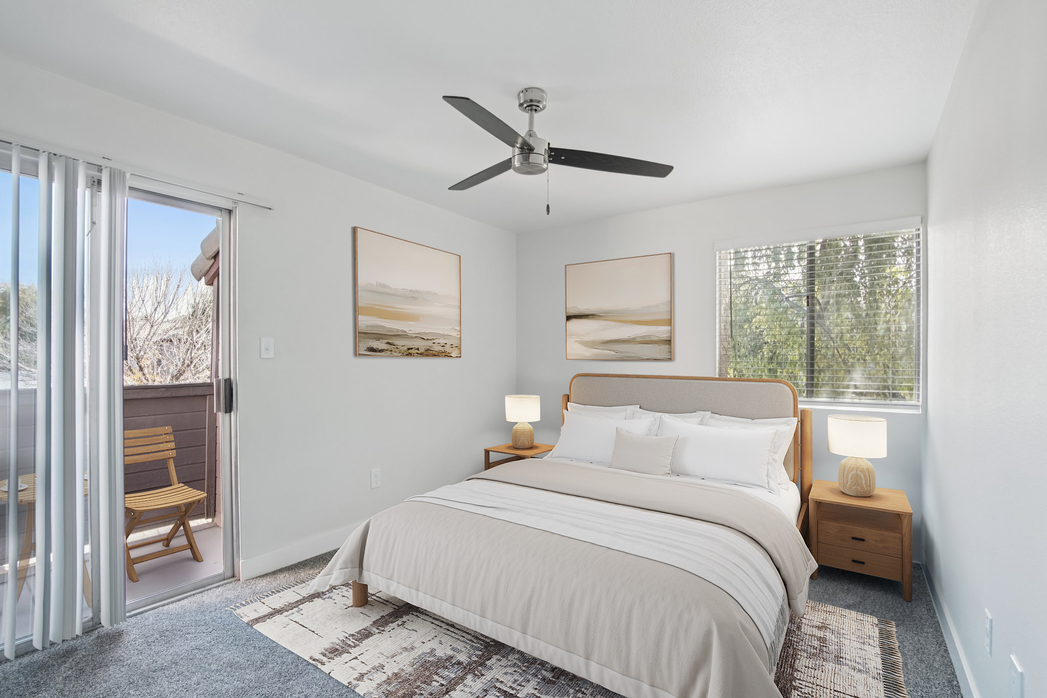A bright and airy bedroom featuring a queen-sized bed with beige and white bedding. There are two wooden nightstands with lamps, a large abstract painting on the wall, and a window with a view. The decor is minimal yet stylish, with a light color palette and a cozy atmosphere.
