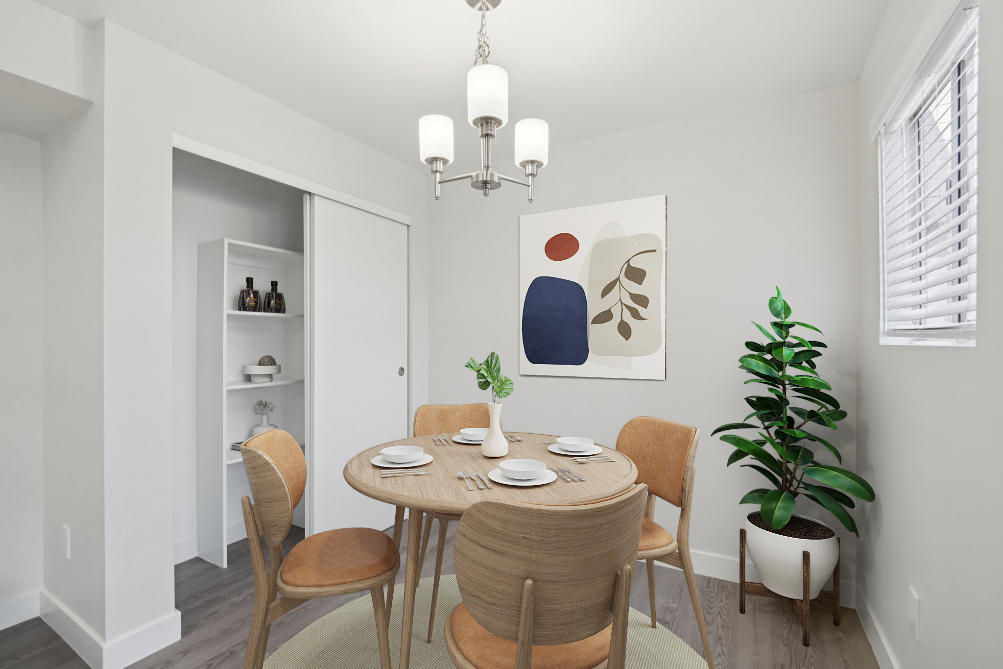 Modern dining area featuring a round wooden table set for four with dishes, surrounded by mid-century style chairs. A large abstract artwork in warm tones hangs on the wall, complemented by a potted plant in the corner. Soft lighting illuminates the bright, minimalist space.