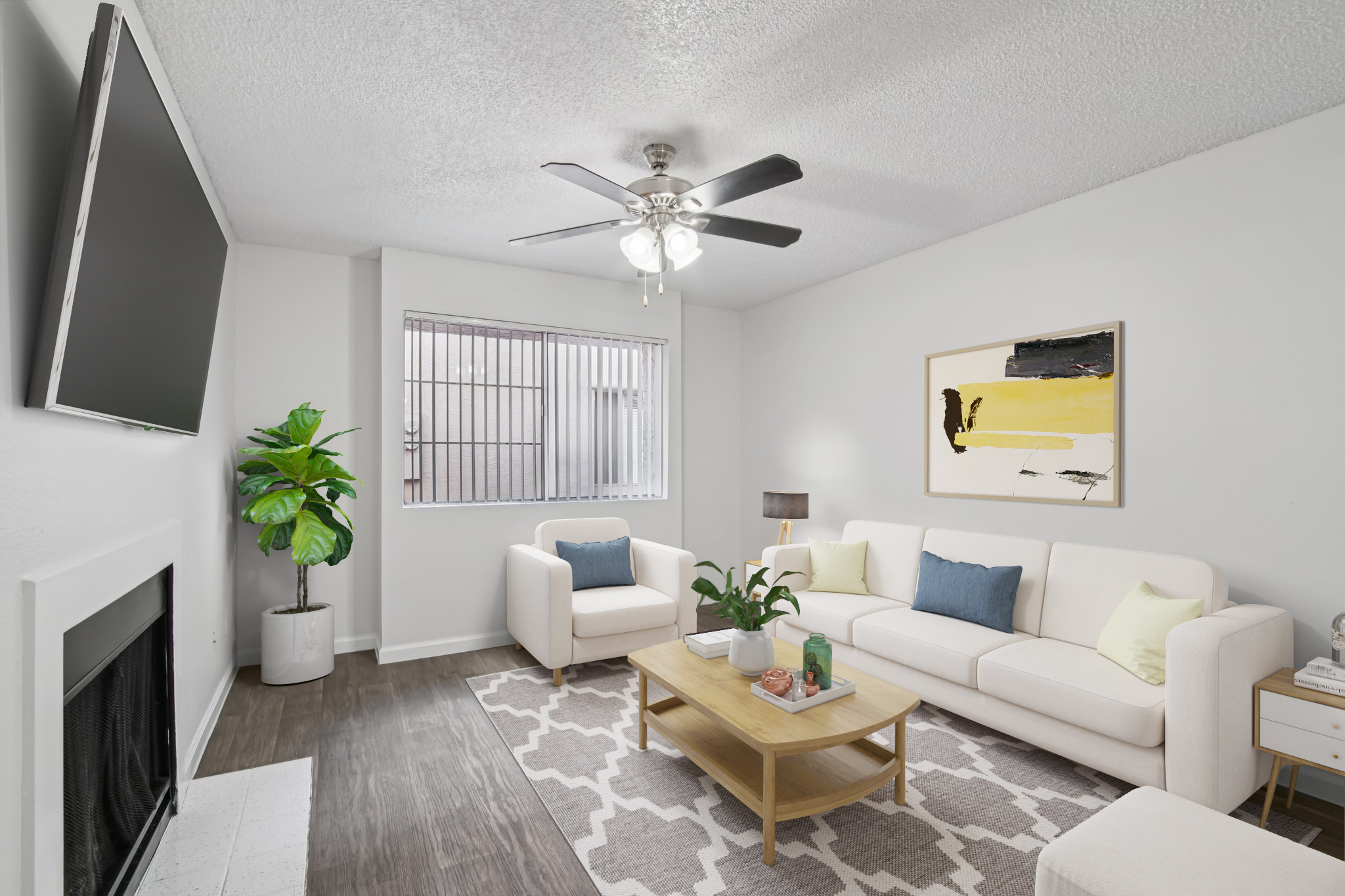 A modern living room featuring a white sofa and armchair, a wooden coffee table with plants, a ceiling fan, and a mounted television. There is a large window with vertical blinds and an abstract painting on the wall. A potted plant adds a touch of greenery to the space. The flooring is dark wood.