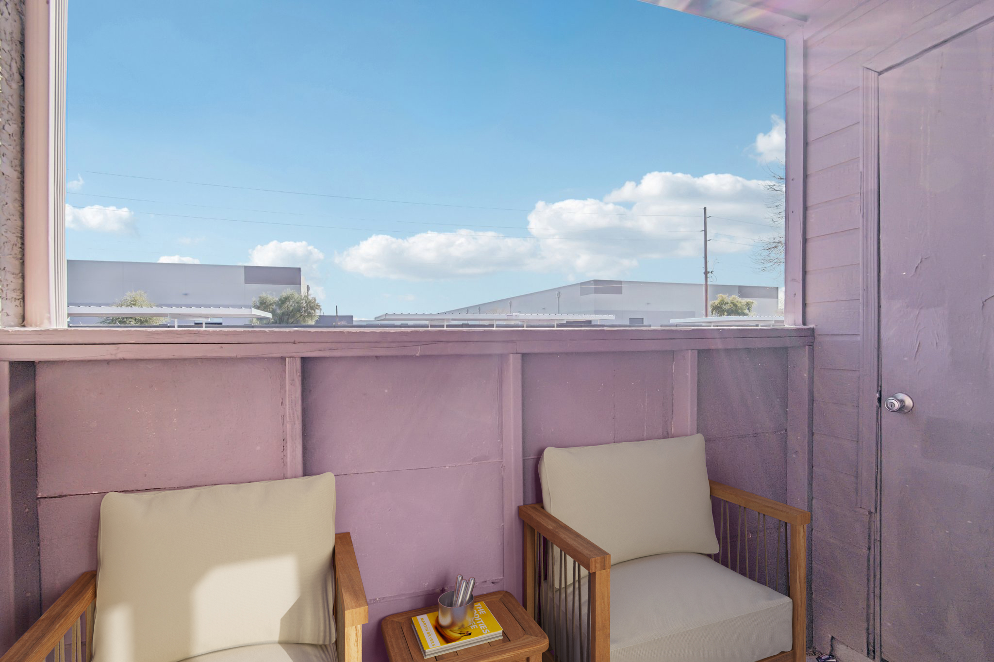A cozy seating area with two light-colored chairs and a small table, overlooking a clear blue sky with fluffy white clouds. The walls are painted in soft purple, enhancing the inviting atmosphere of the space, perfect for relaxation and enjoying the view.