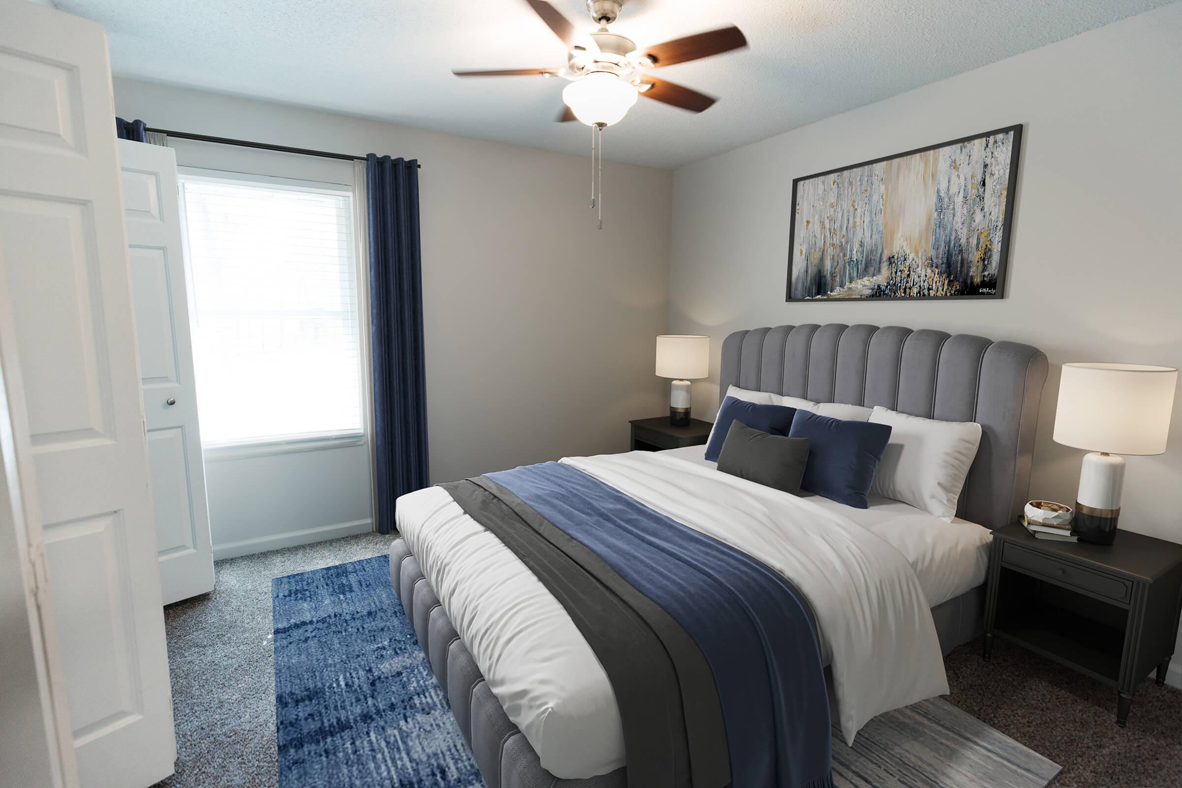 A well-decorated bedroom featuring a plush gray bed with blue and white bedding. Flanking the bed are two nightstands with table lamps. A large window with gray curtains allows natural light to illuminate the space. A piece of abstract art hangs above the bed, adding a touch of color to the neutral walls.