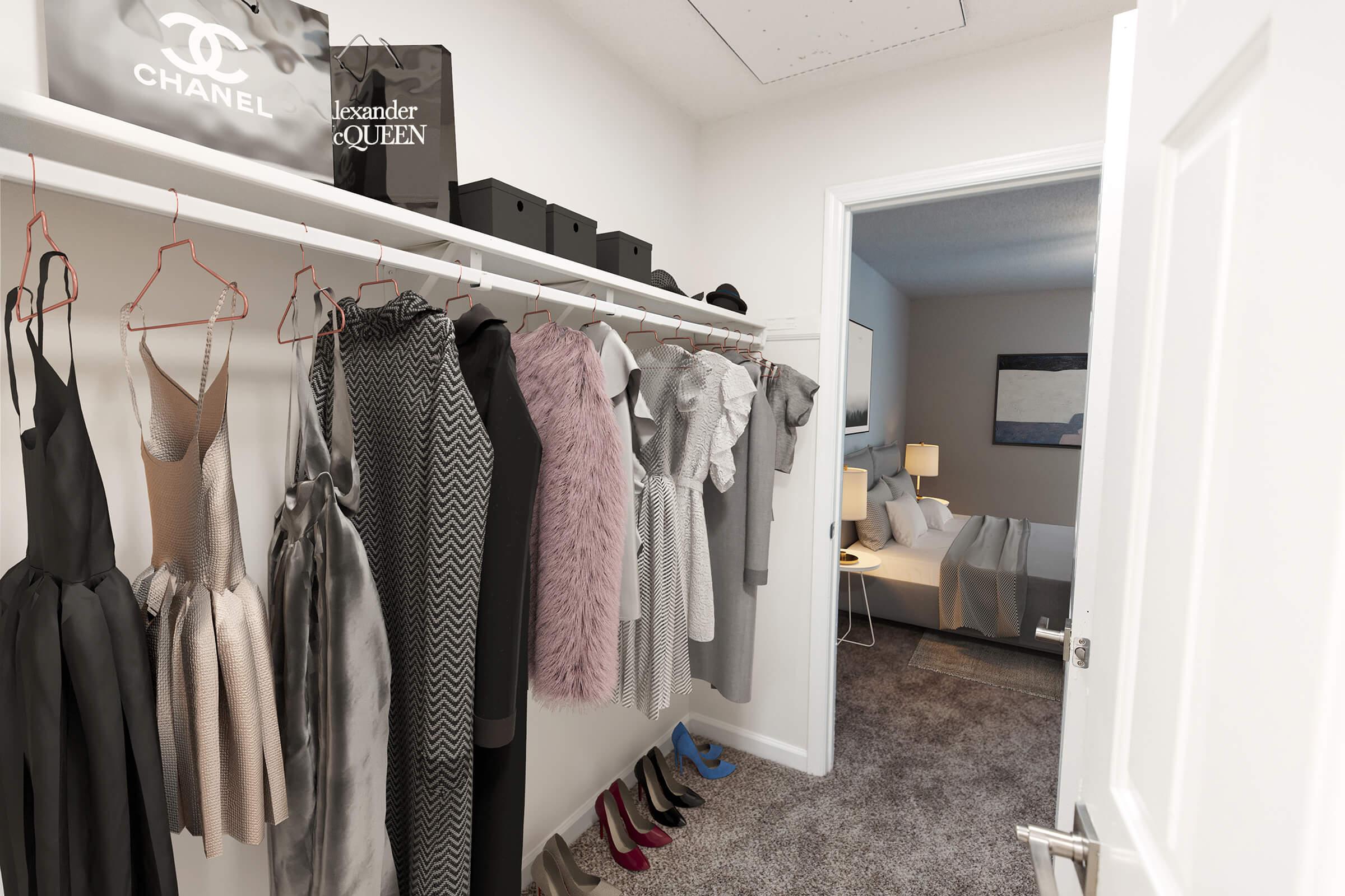 A spacious walk-in closet featuring a variety of stylish women's clothing on hangers, including dresses and a fuzzy coat. Black and gray boxes are neatly arranged on the shelf. The closet opens to a well-decorated bedroom with a bed and lamps visible in the background. Soft lighting enhances the inviting atmosphere.