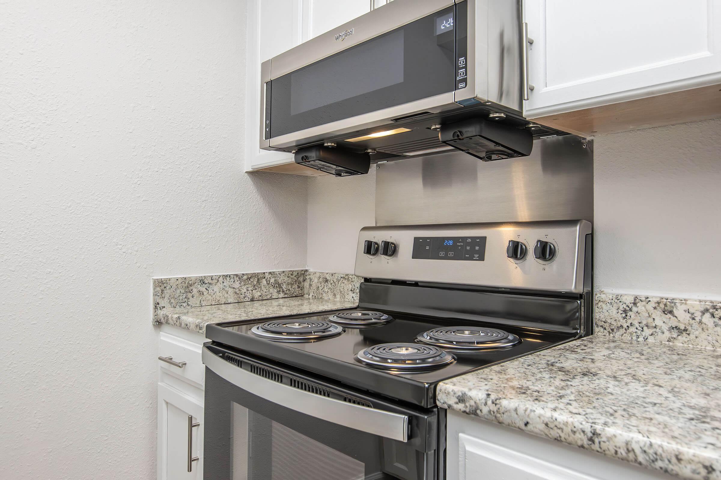 A modern kitchen featuring a stainless steel electric stove with four burners, an overhead microwave, and granite countertops. The white cabinets provide a clean, bright look to the space, with a focus on functionality and style.