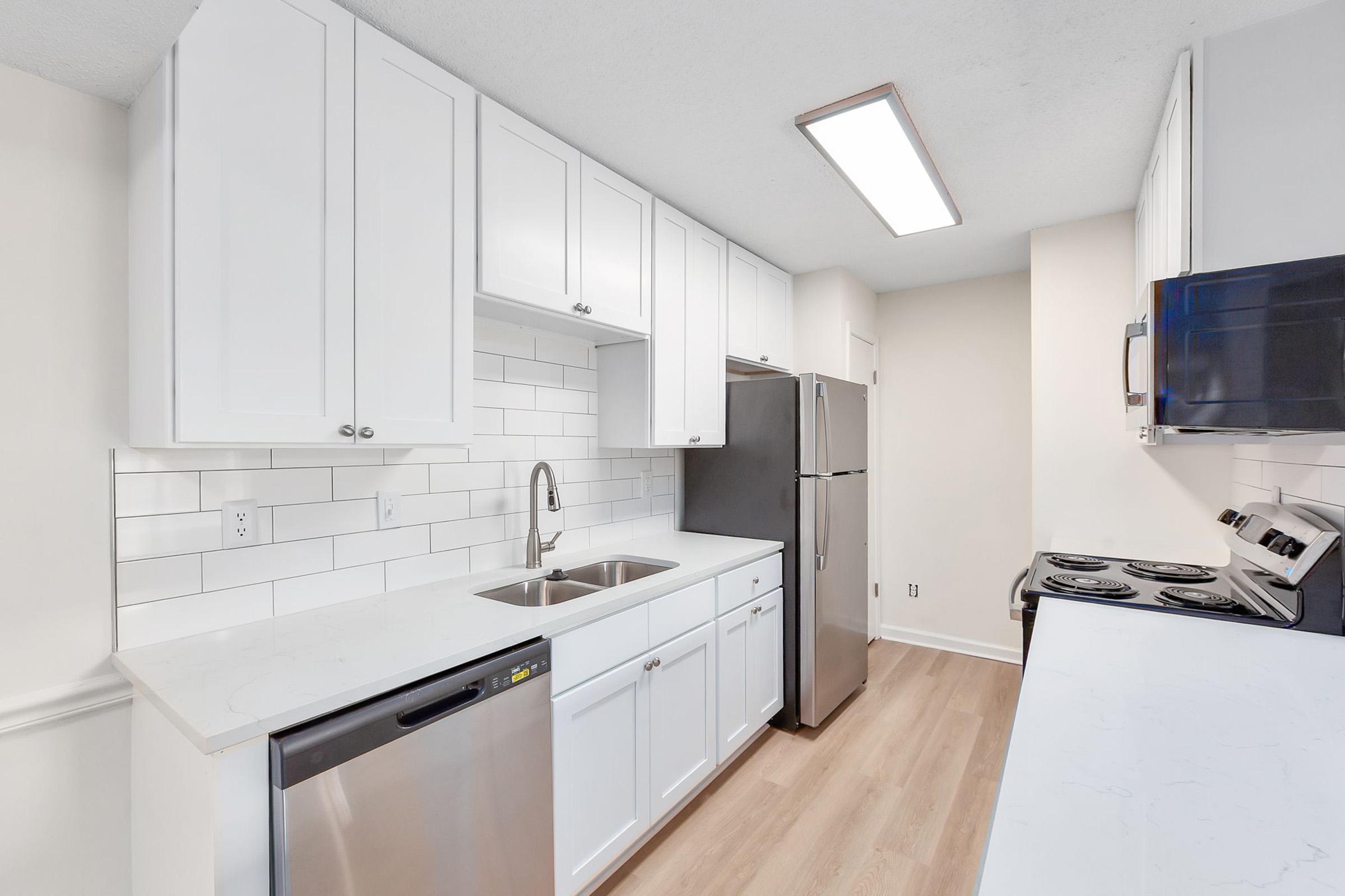 A modern kitchen featuring white cabinets, stainless steel appliances, and a light-colored countertop. The layout includes a double sink, a dishwasher, a refrigerator, and a stove with an oven, all set against a stylish backsplash with white tiles. Natural light enhances the spacious feel.