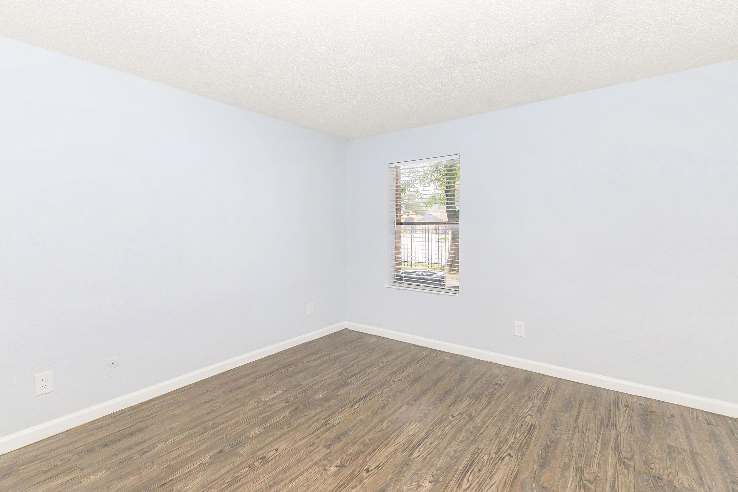 A light blue room with wooden flooring and a single window. The walls are painted a soft blue, and the room appears empty, providing a spacious and inviting atmosphere. Natural light enters through the window, enhancing the bright and airy feel of the space.