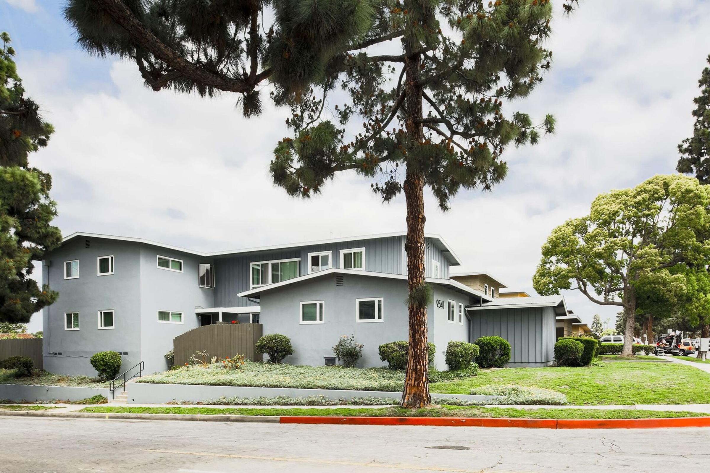 Two-story apartment building surrounded by landscaping with a tree in the foreground