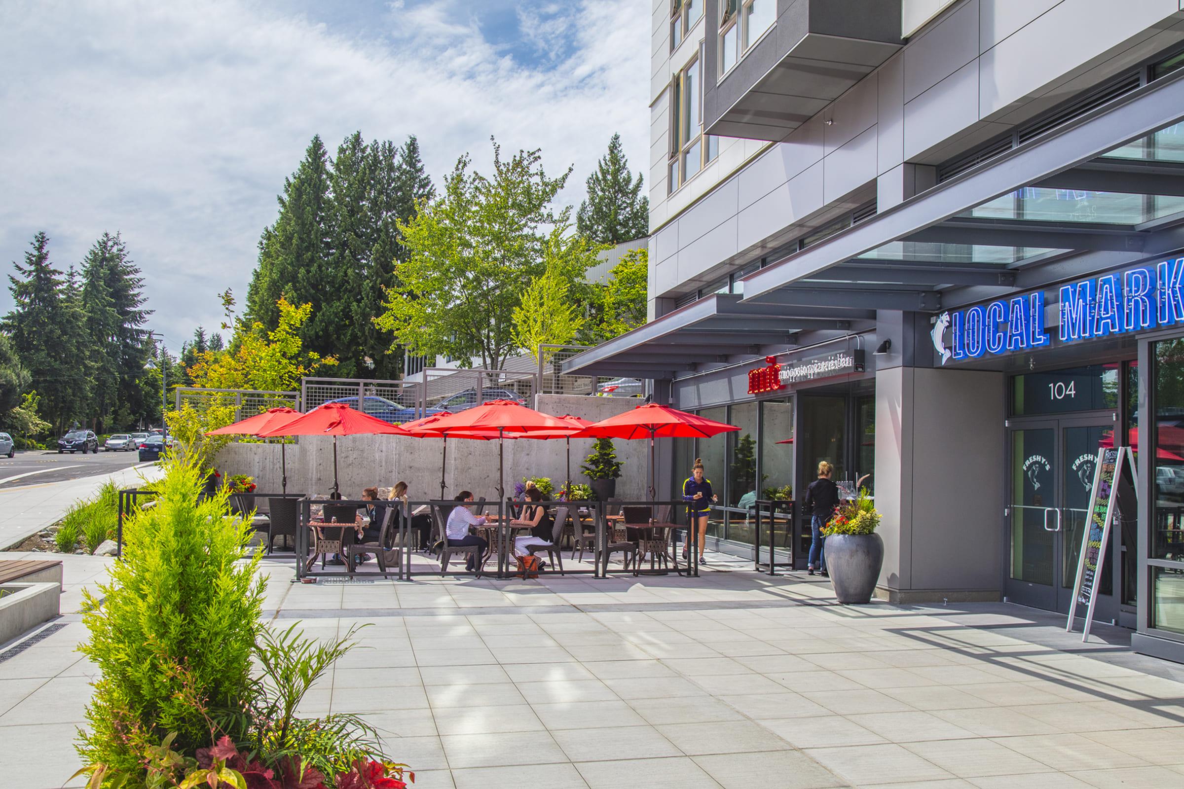 Outdoor seating area of a café or restaurant with red umbrellas, surrounded by greenery.