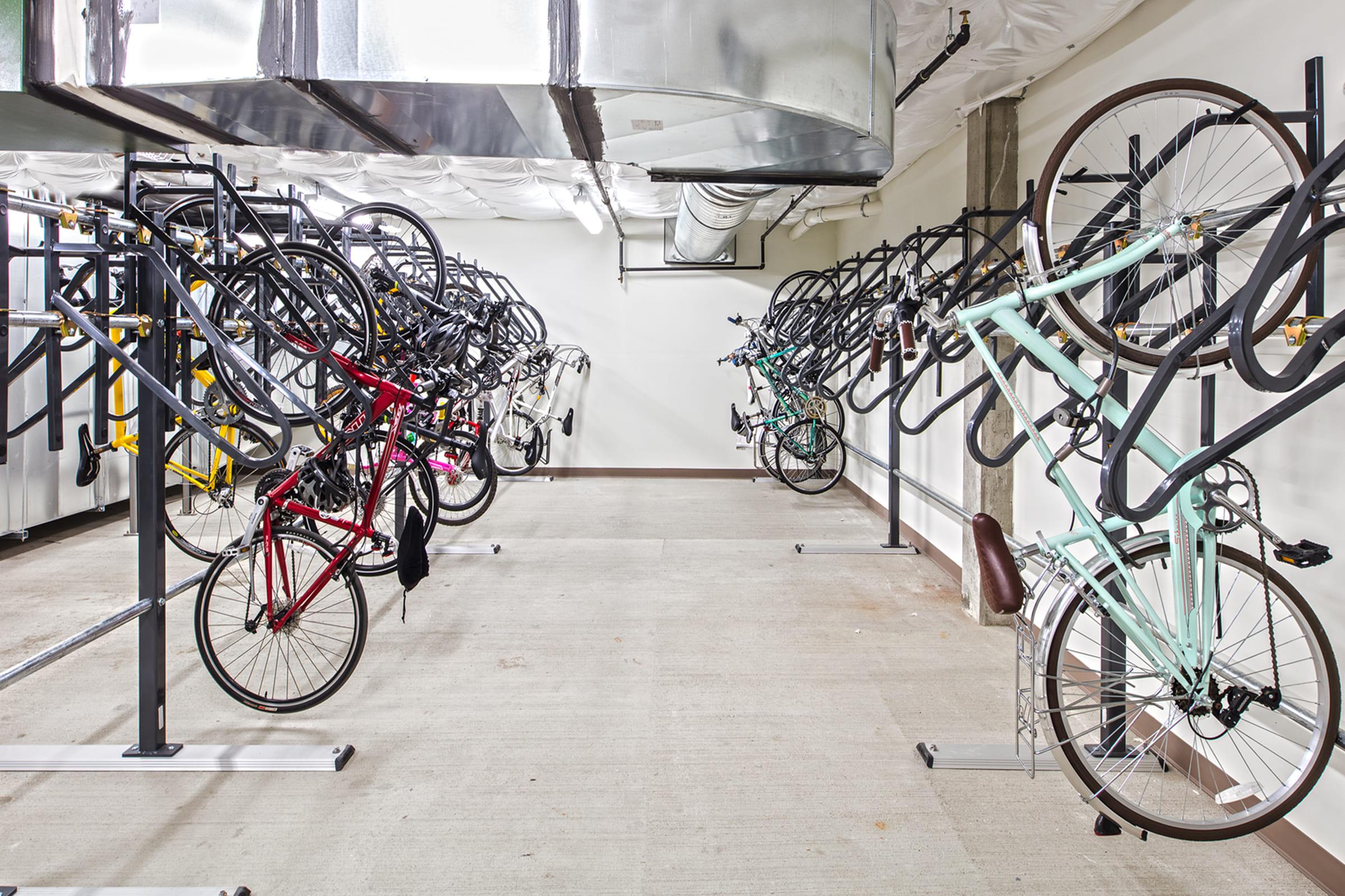 A well-organized bike storage area featuring multiple bicycles hanging on racks. The space has a clean, industrial look with metal air ducts overhead and a concrete floor, providing an efficient environment for storing bikes.