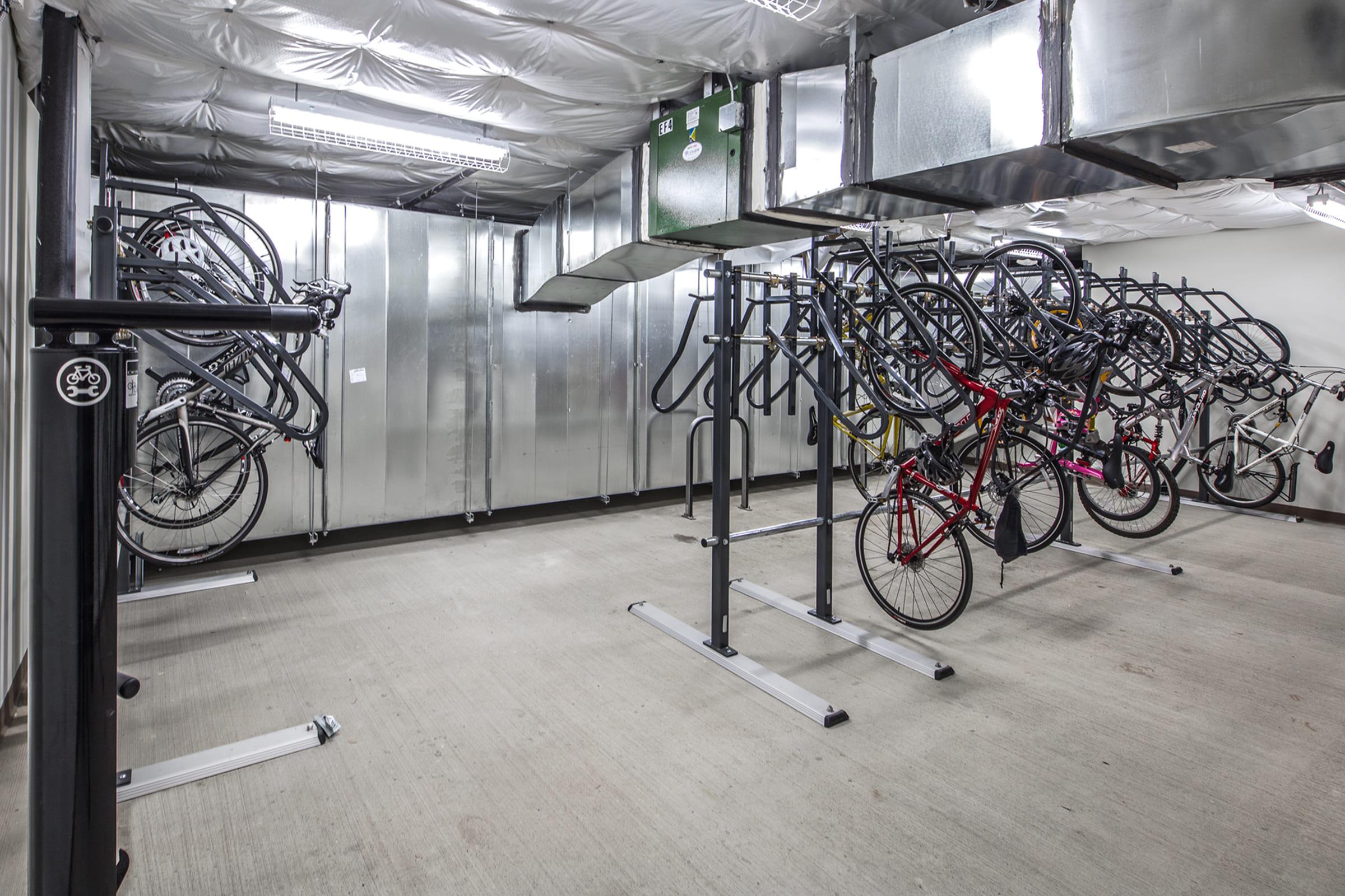 A well-organized indoor bike storage area featuring several mounted bike racks. Various bicycles are neatly hung, showcasing a mix of colors and styles. The space is equipped with metallic walls and ceilings, providing a clean and functional environment for bike storage.