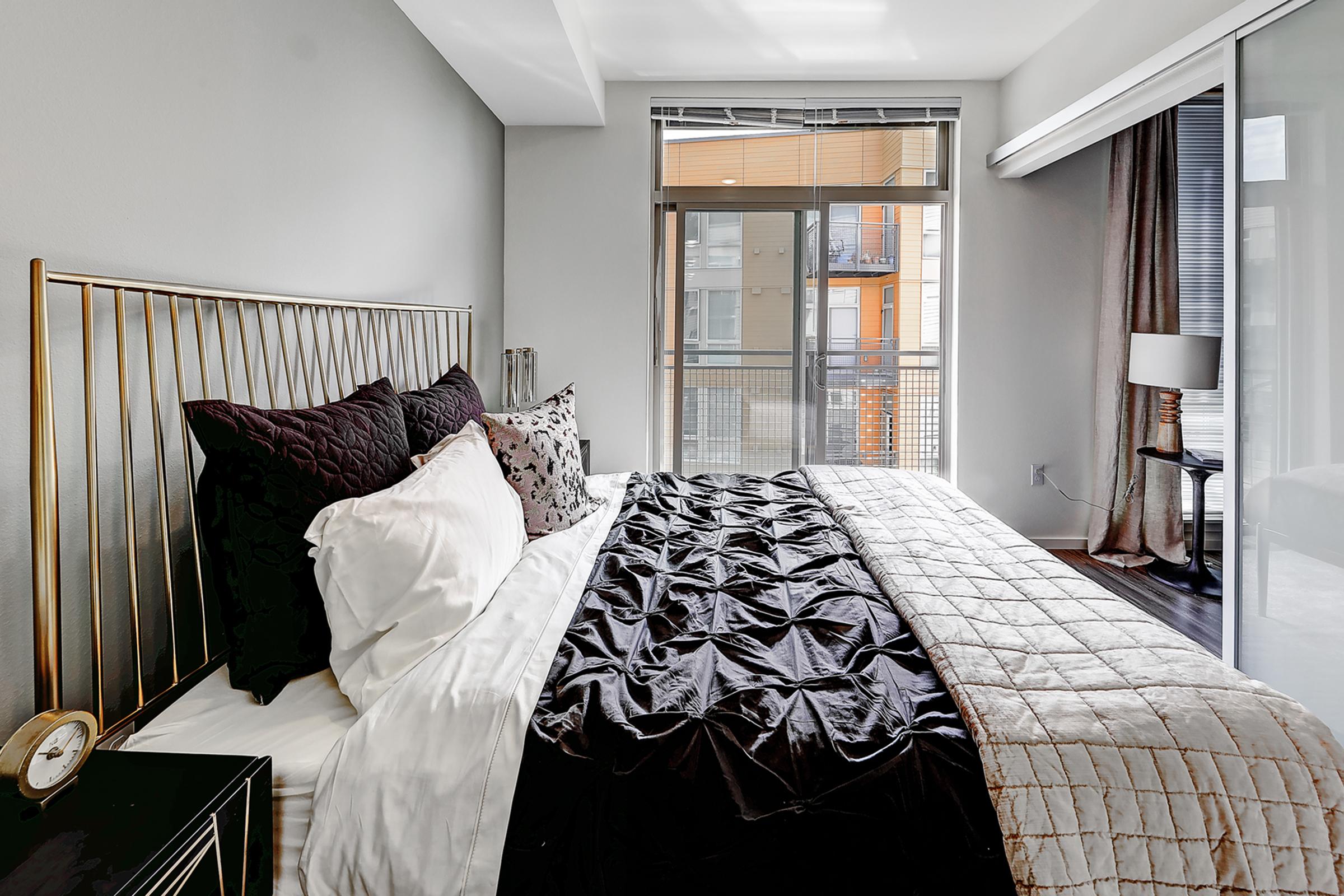 A modern bedroom featuring a stylish bed with black and white bedding, a decorative pillow, and a bedside table with a clock.
