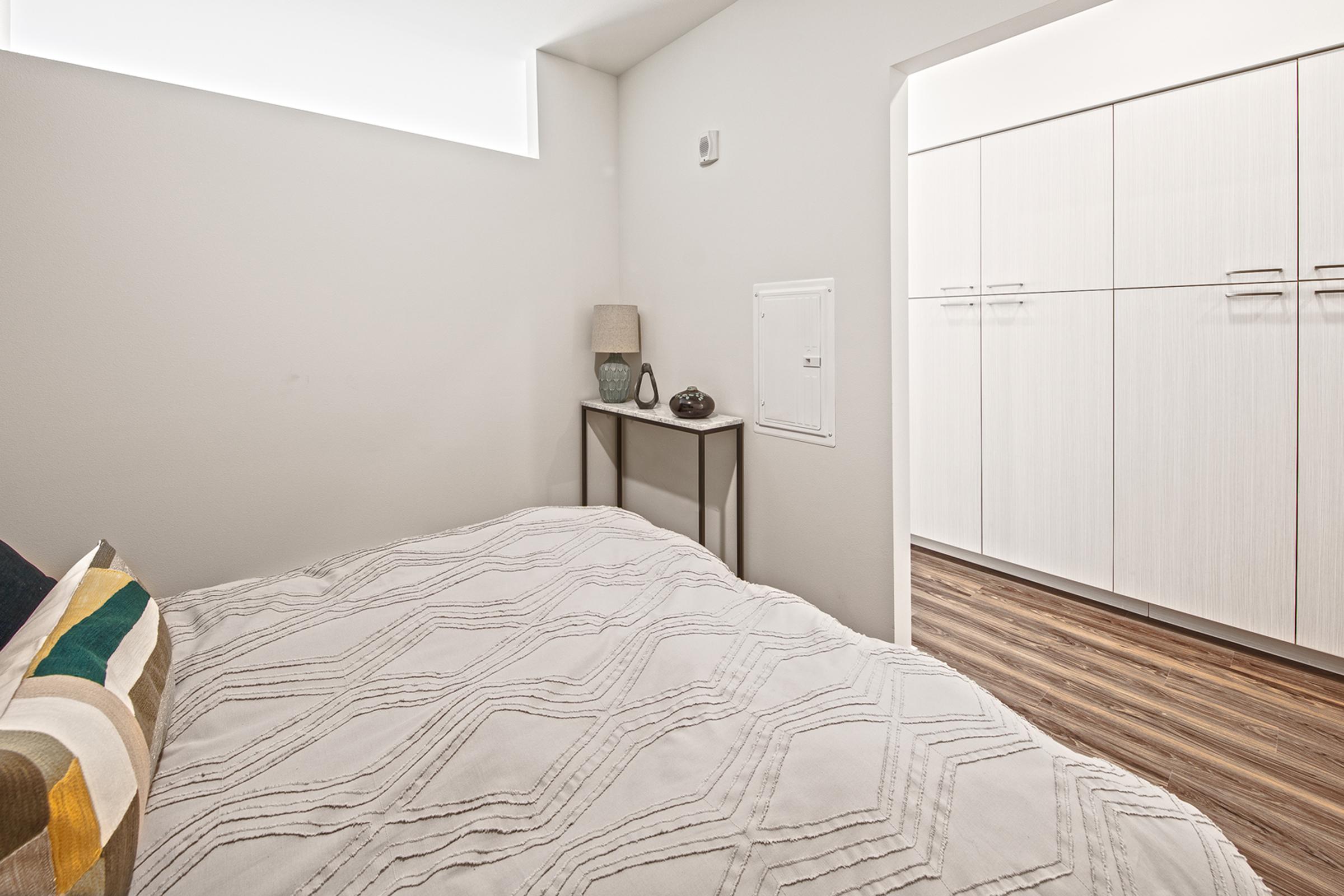 A cozy bedroom featuring a neatly made bed with a textured white blanket and a colorful decorative pillow.