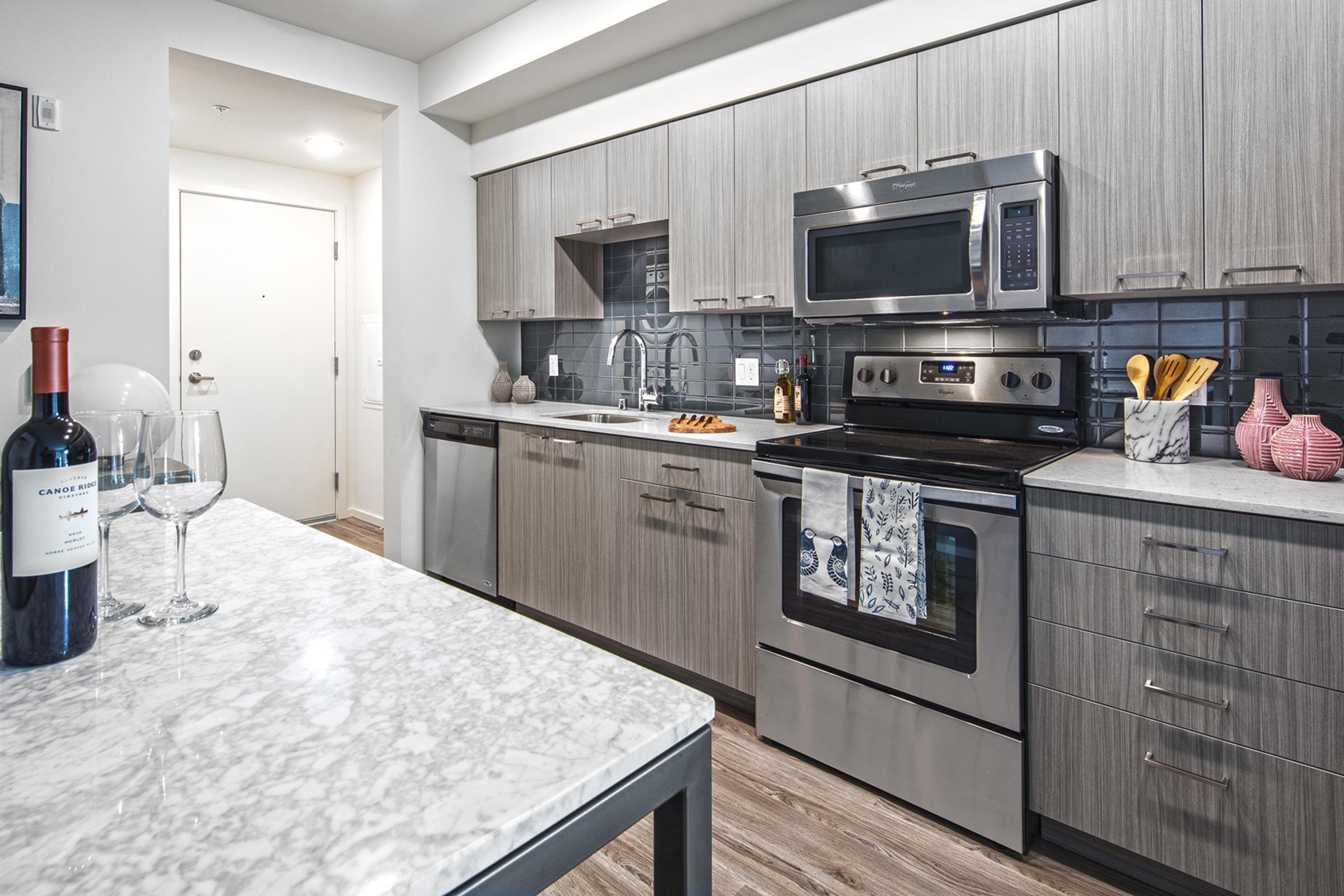 Modern kitchen featuring stainless steel appliances, including an oven and microwave, with a marble countertop and wooden cabinetry.