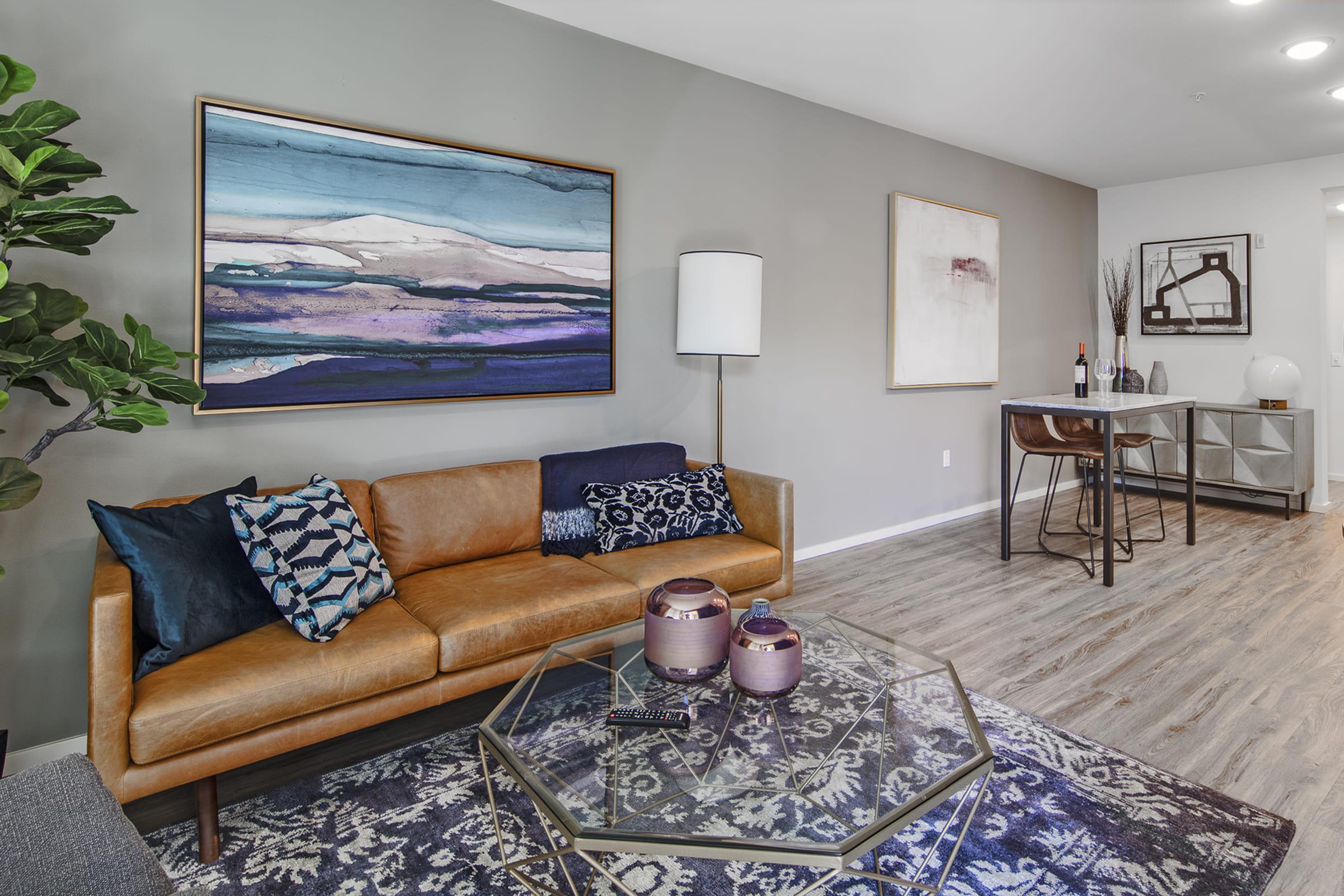 A modern living room featuring a brown leather sofa adorned with decorative pillows, a geometric coffee table with decorative items, and abstract wall art.