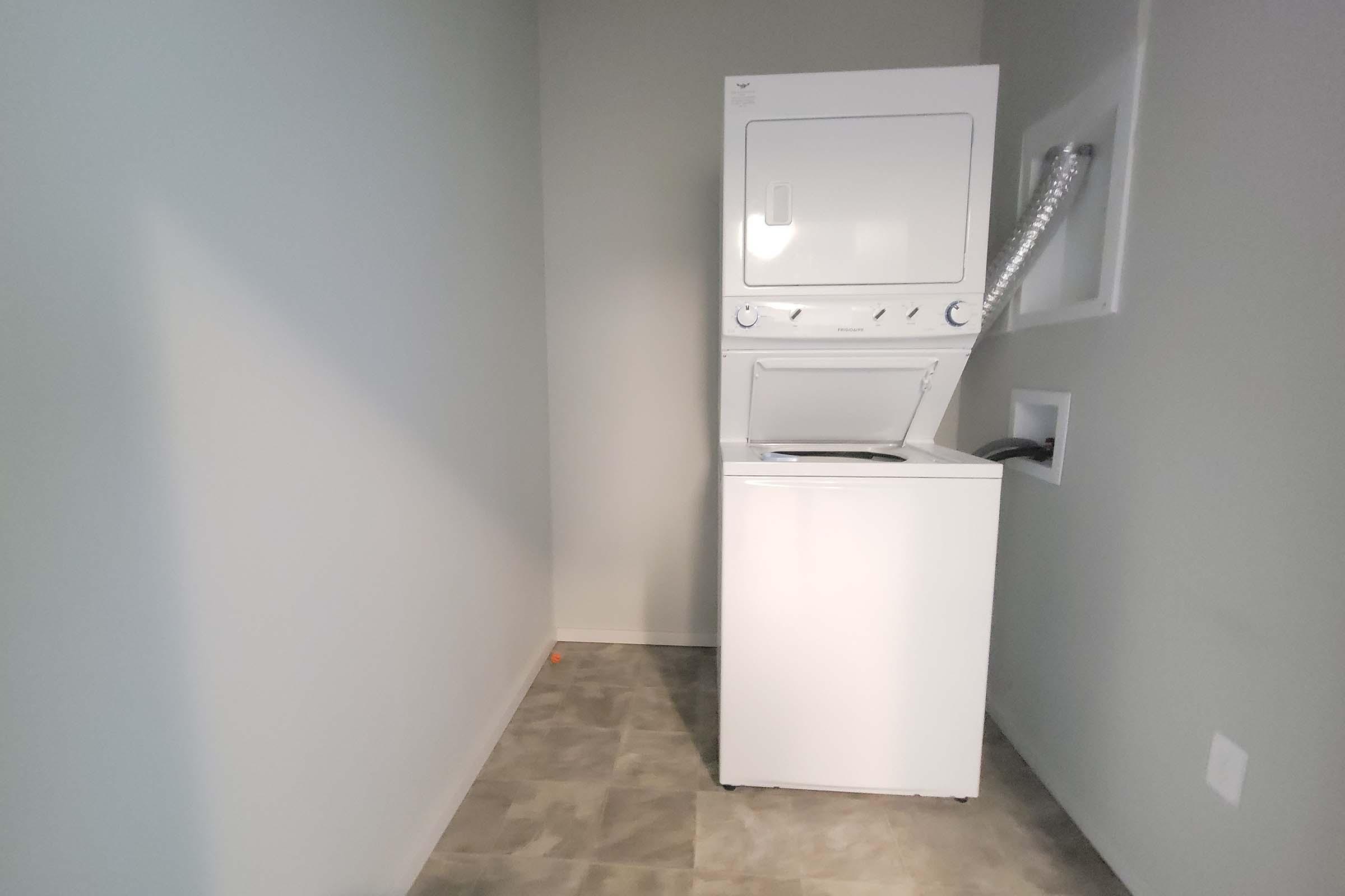 A stackable washer and dryer unit in a small laundry area with light-colored walls and tiled flooring. The space appears clean and uncluttered, providing a functional area for laundry tasks.