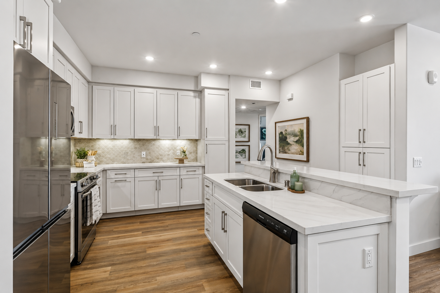 Modern kitchen with white cabinetry, a marble countertop, and a stainless steel refrigerator. Features include an oven, sink, and dishwasher, with warm wood flooring and soft lighting. Decorated with small plants and artwork on the walls, creating a bright and inviting atmosphere.