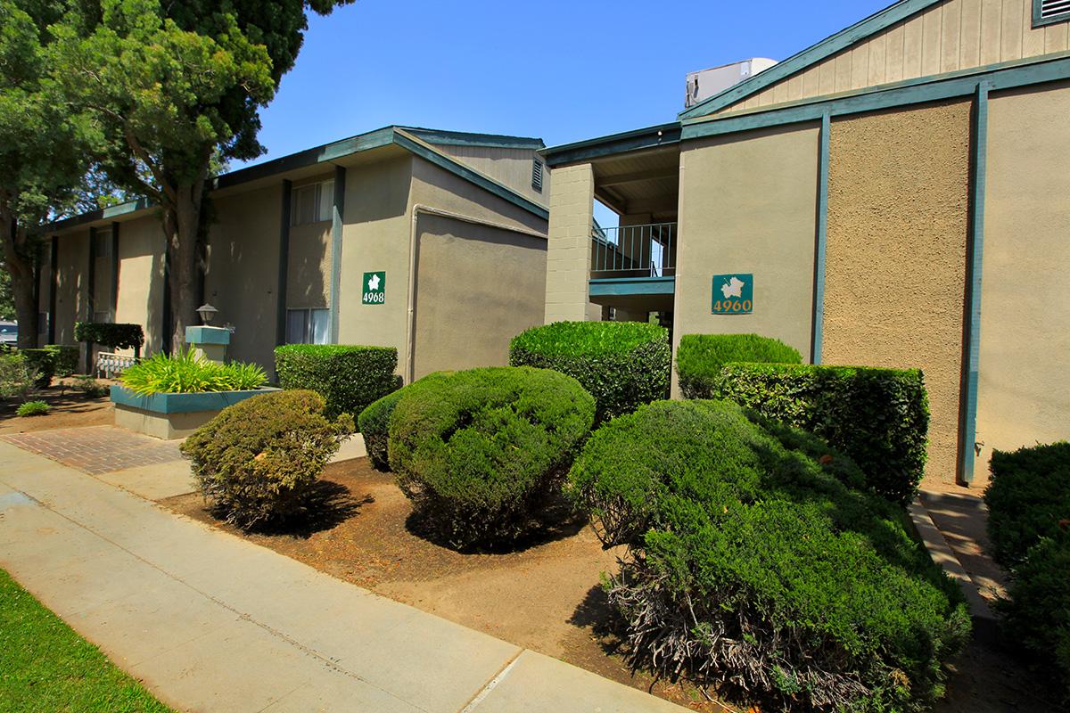 shrub trees and sidewalk in front of a two story building.