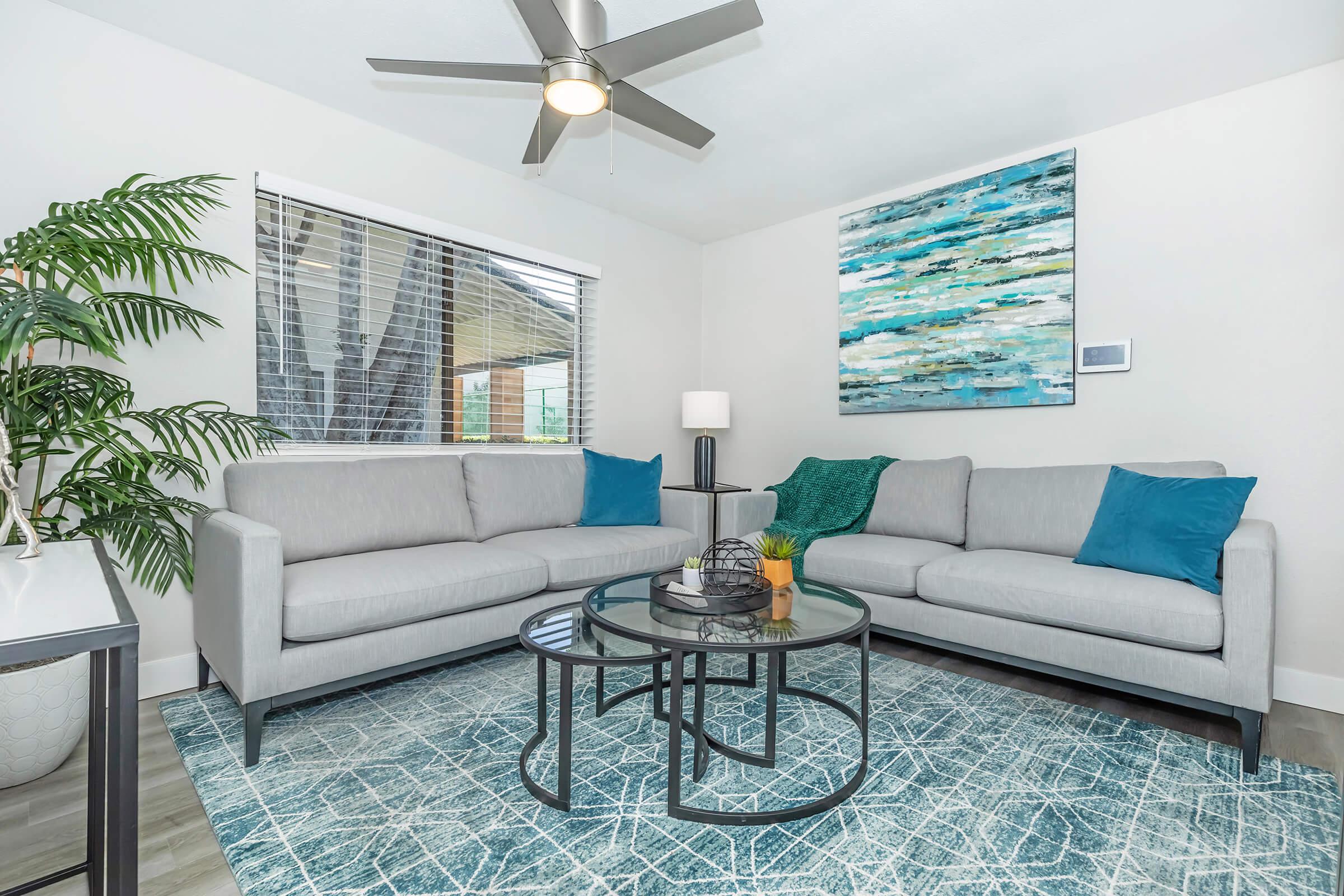 Phoenix, AZ Luxury Apartments For Rent - Tides on 71st - Blue-Themed Living Room with Couches, Painting, Window, and Ceiling Fan