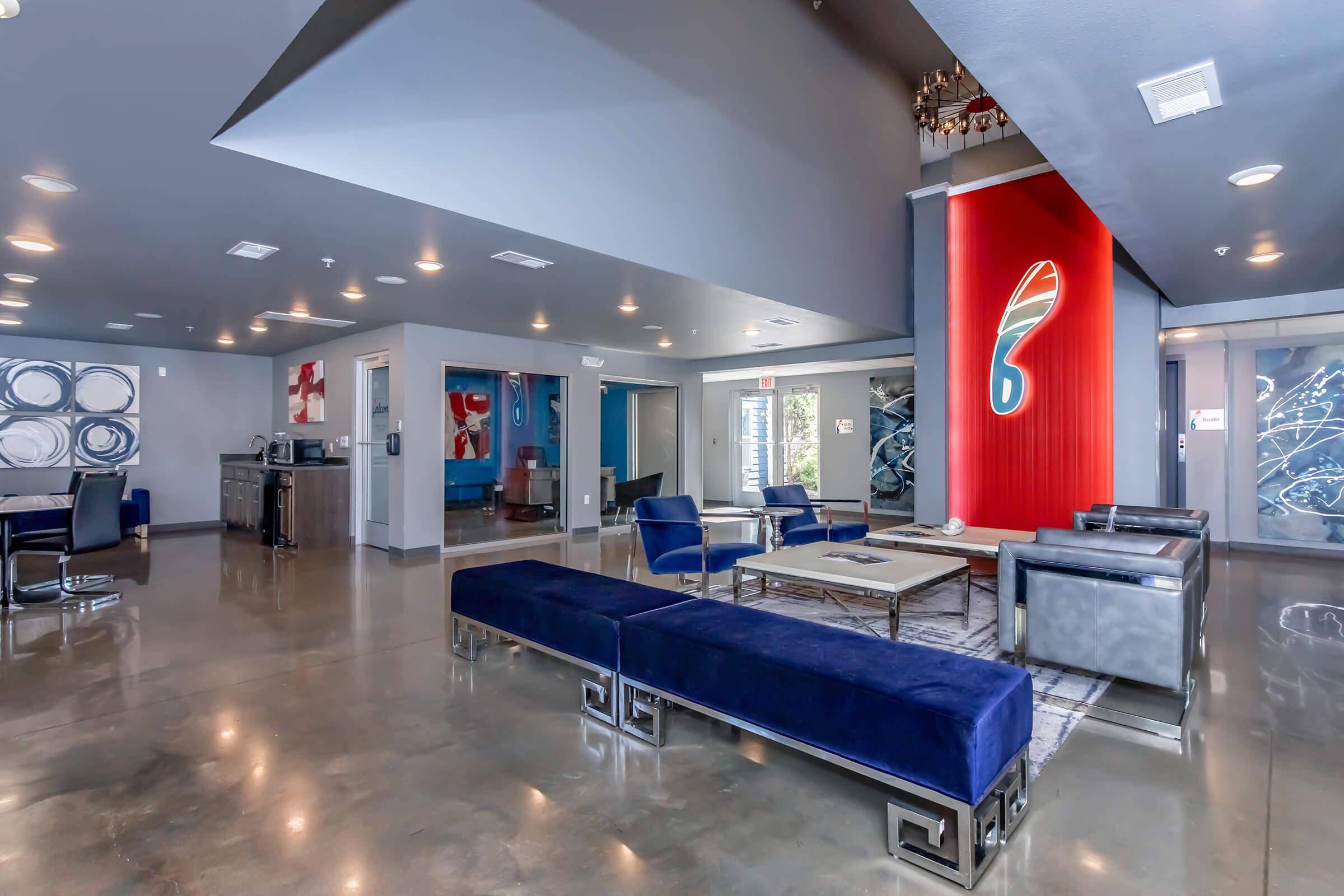 Modern lounge area featuring blue upholstered seating, a coffee table, and contemporary artwork on the walls. The space is well-lit with a mix of natural and artificial lighting, showcasing polished concrete flooring and stylish decor elements.
