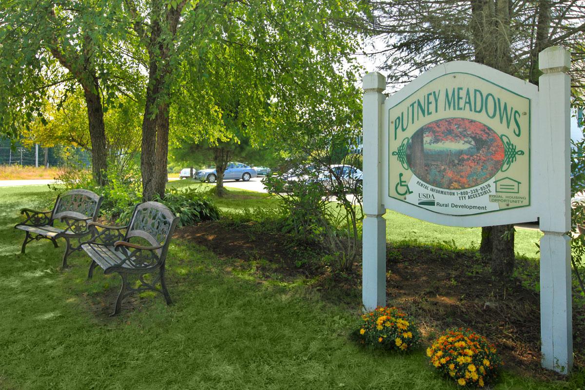 a sign over a grassy area with trees in the background