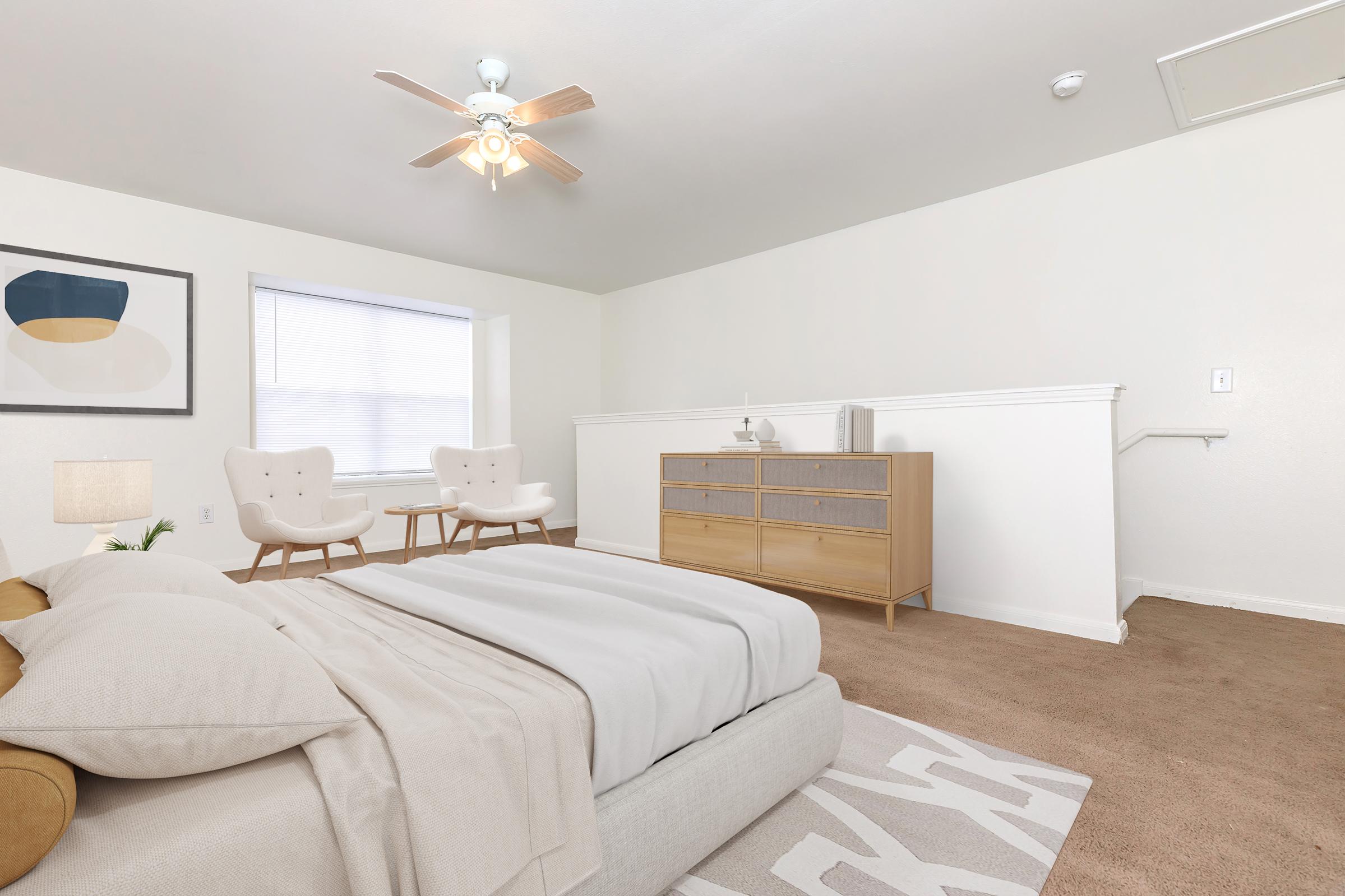 Bright and airy bedroom featuring a comfortable bed with neutral bedding, two modern accent chairs, a stylish dresser with storage, and a ceiling fan. Natural light streams through a window, and a framed artwork adds a touch of decor to the minimalist space.