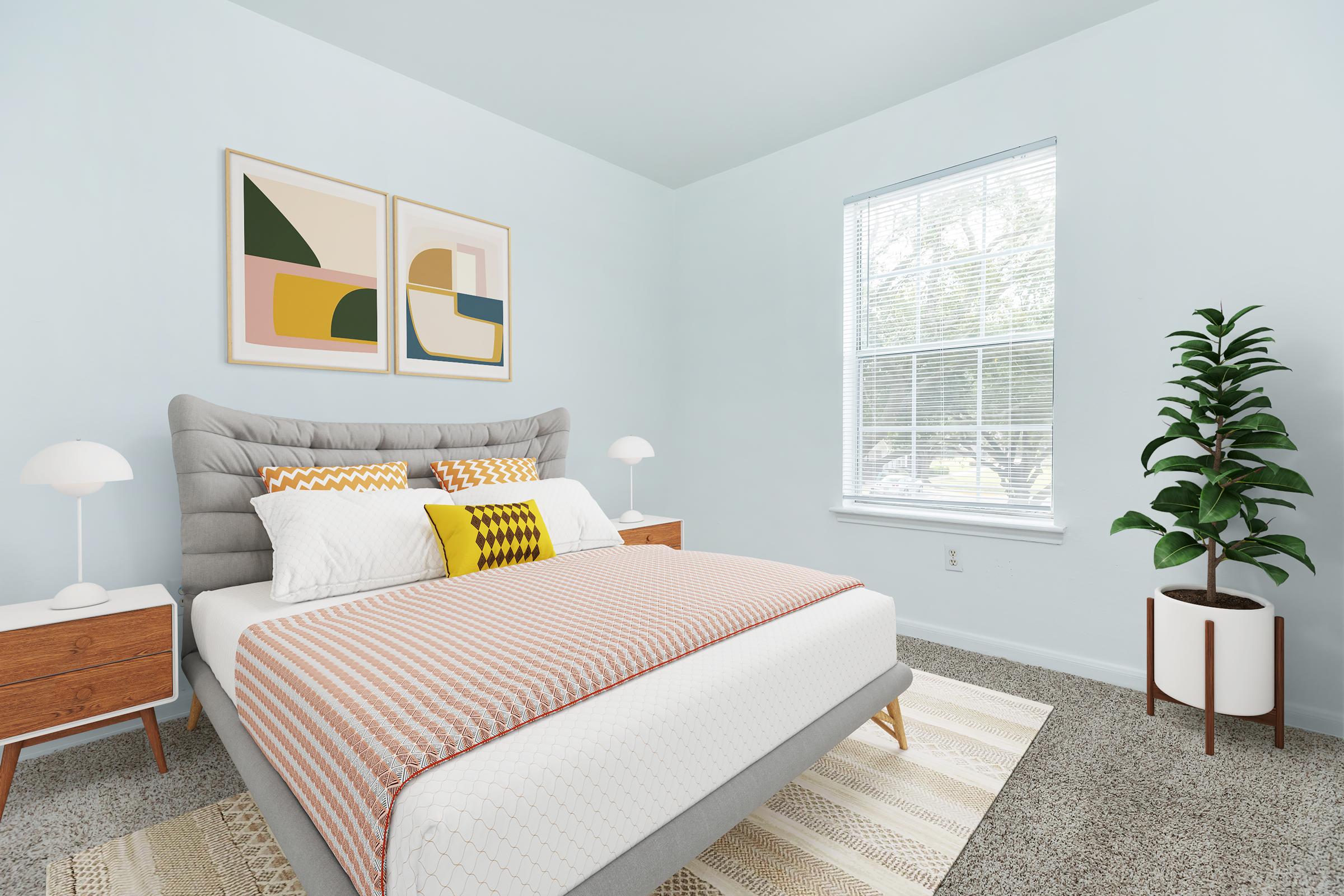 A softly lit bedroom featuring a grey upholstered bed with a white and coral striped blanket. There are two decorative pillows on the bed, alongside stylish nightstands with modern lamps. Wall art in muted colors hangs above the bed, and a tall green plant is placed in a white pot near a window.