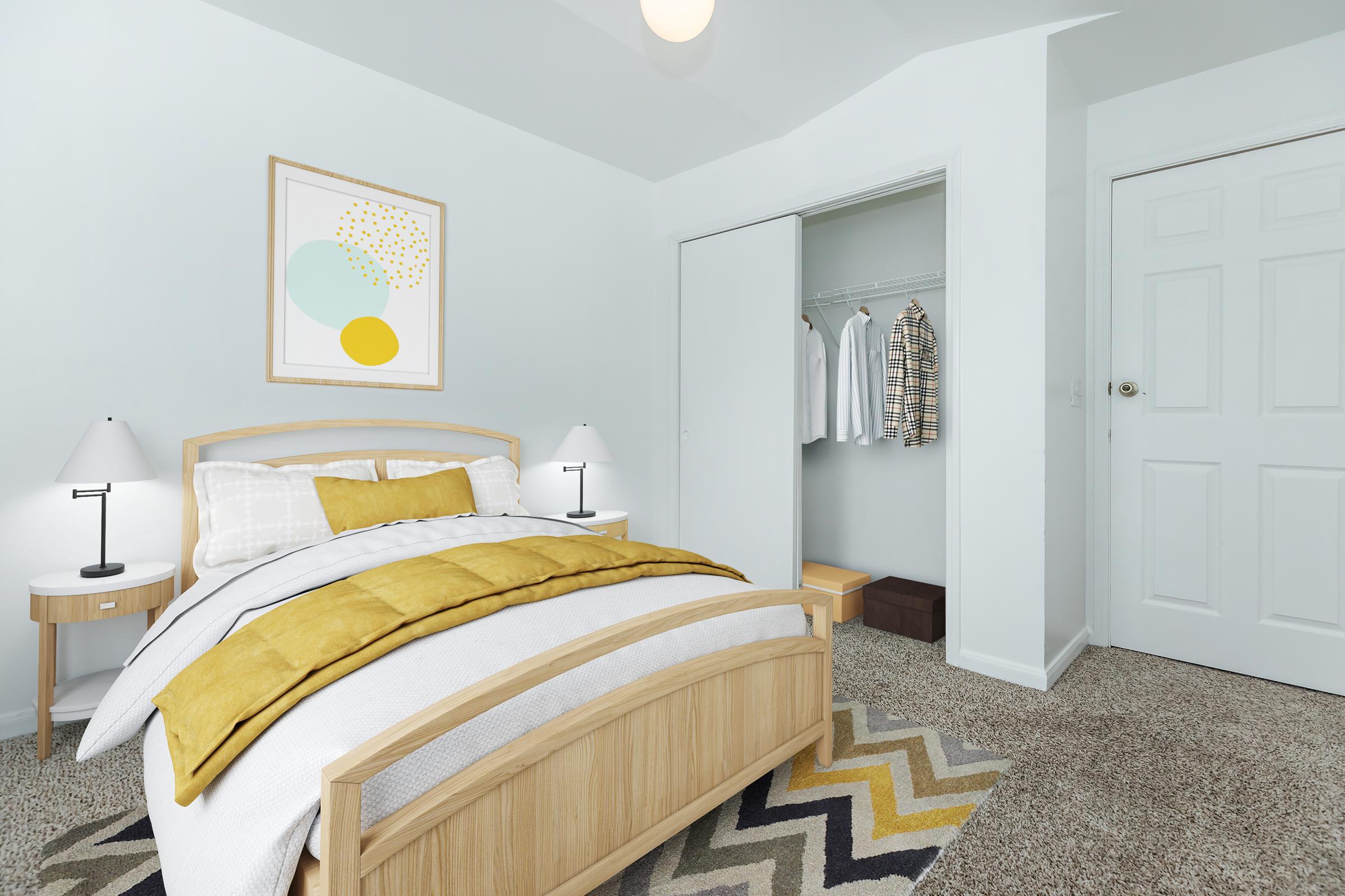 A well-decorated bedroom featuring a wooden bed with white and yellow bedding, two bedside lamps on matching nightstands, and a cozy triangular-patterned rug. A closet is partially open, displaying hanging clothes and storage boxes, with light walls and a simple framed artwork above the bed.