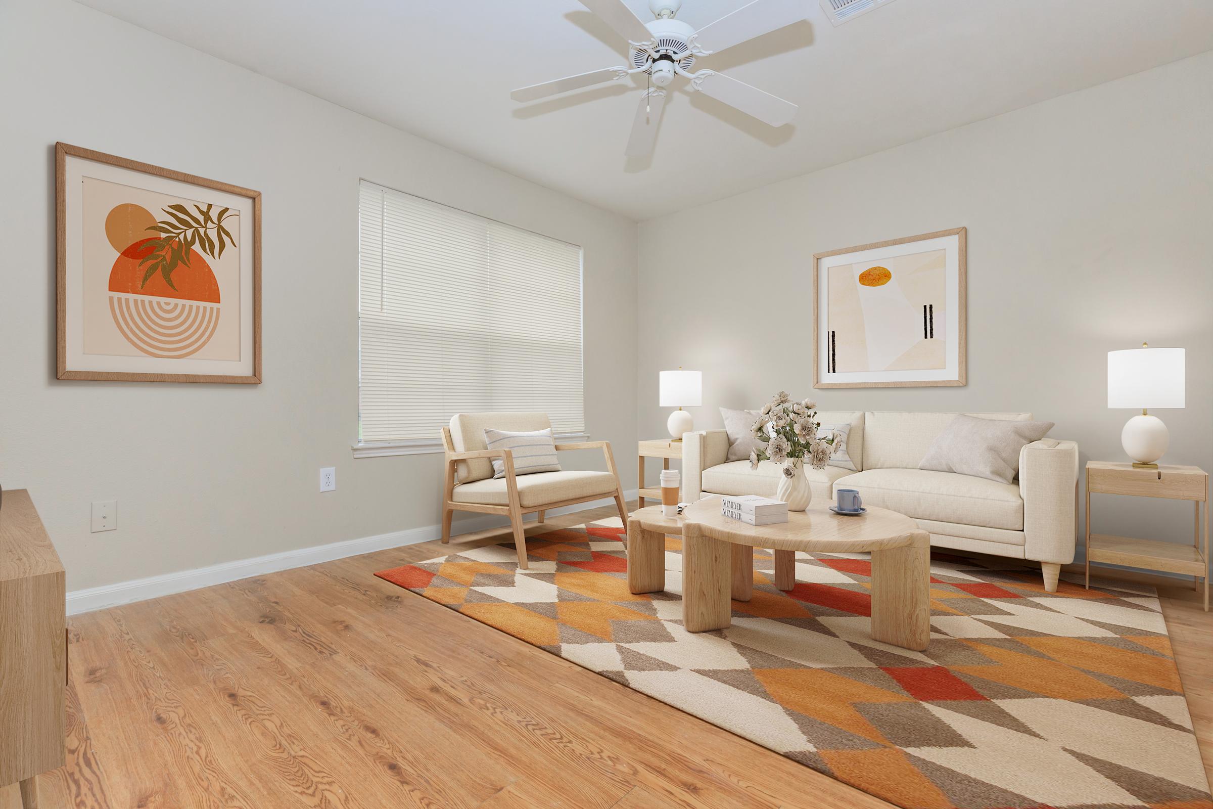 A cozy living room featuring a light-colored sofa, wooden furniture, and a decorative area rug with geometric patterns. Two lamps provide soft lighting, and artwork hangs on the walls, adding a modern touch. A potted plant and a vase with flowers are placed on the coffee table. Natural light filters in through the window.