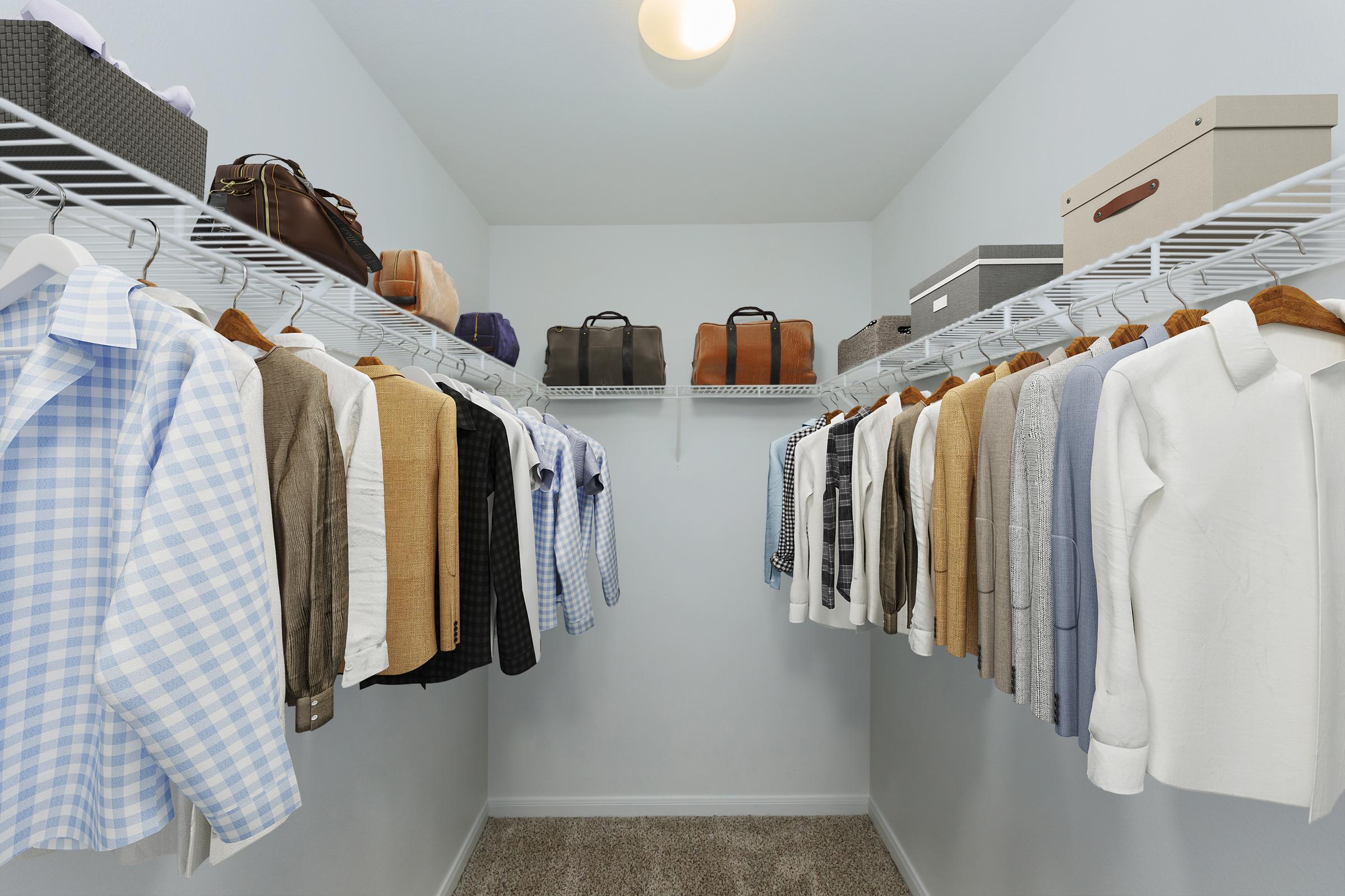 A neatly organized closet featuring a variety of clothing items on hangers, including shirts, jackets, and blazers in different colors and patterns. There are also several bags and storage boxes on shelves above, with a soft carpeted floor and light-colored walls enhancing the clean and spacious feel.