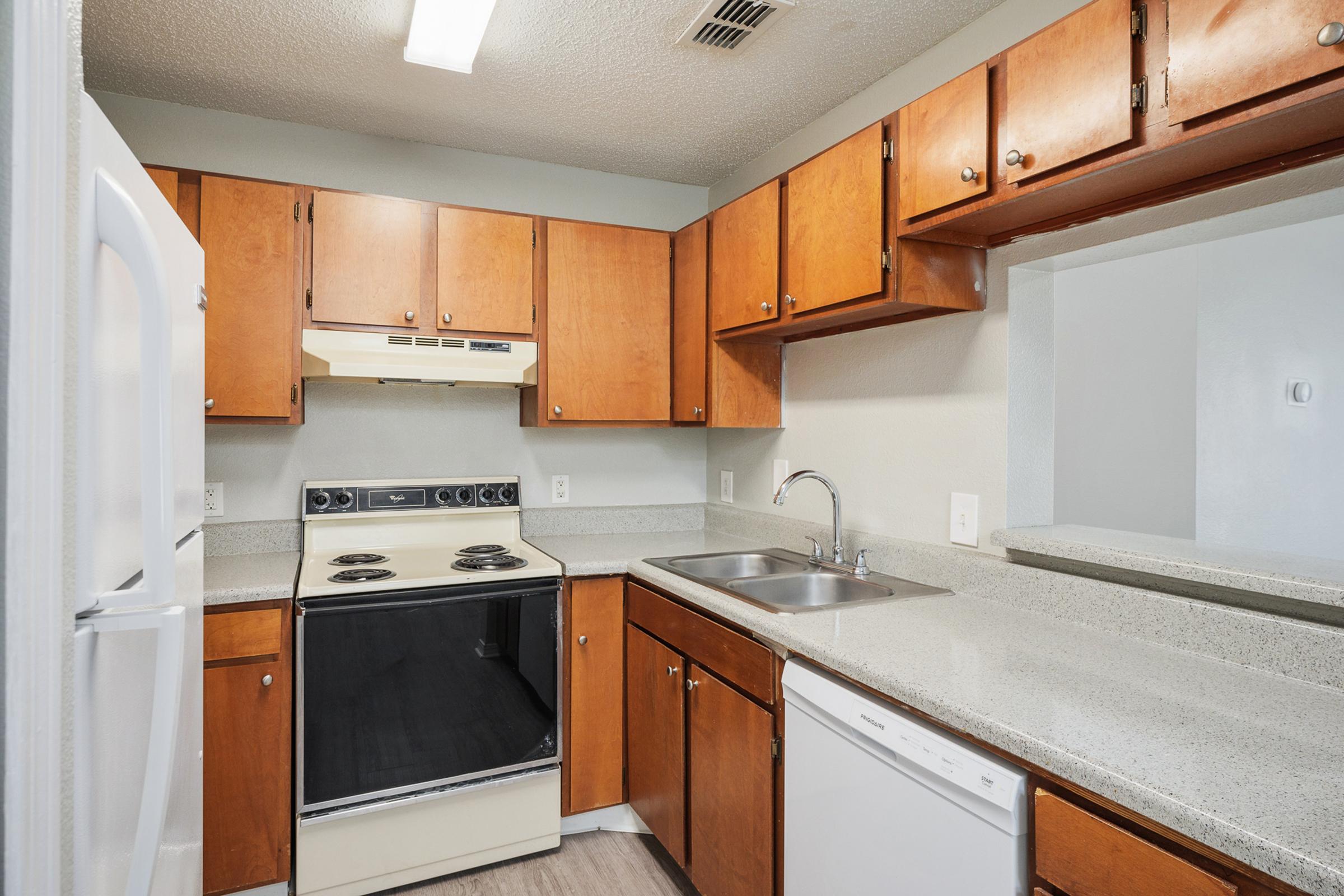 A modern kitchen featuring wooden cabinets, a white refrigerator, a black stove with an oven, a double sink, and a dishwasher. The countertop is light-colored granite, and the walls are painted in soft tones, creating a bright and inviting atmosphere.