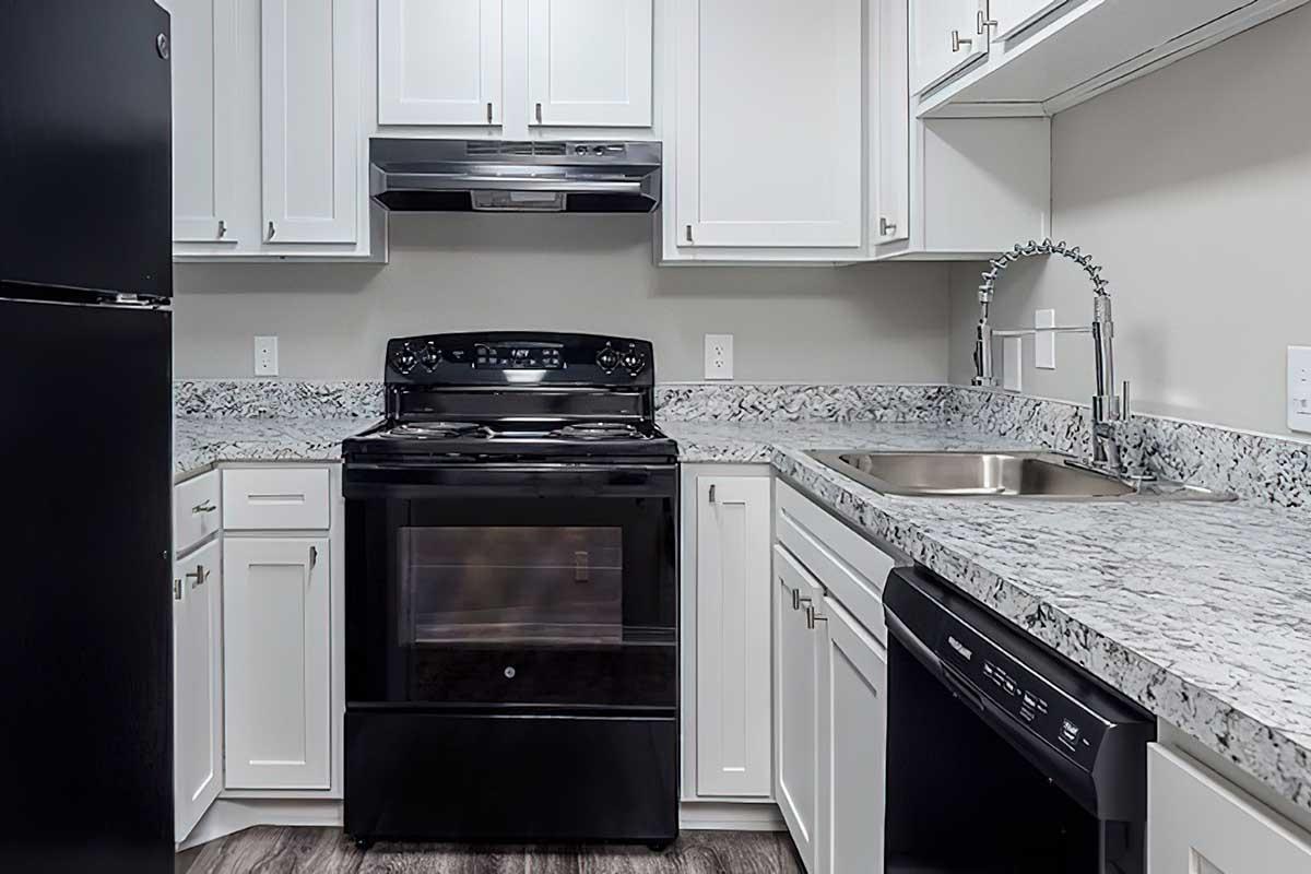 Modern kitchen featuring white cabinetry, black appliances including a stove, refrigerator, and dishwasher, with a granite countertop and stainless steel sink. The design emphasizes clean lines and a contemporary aesthetic.