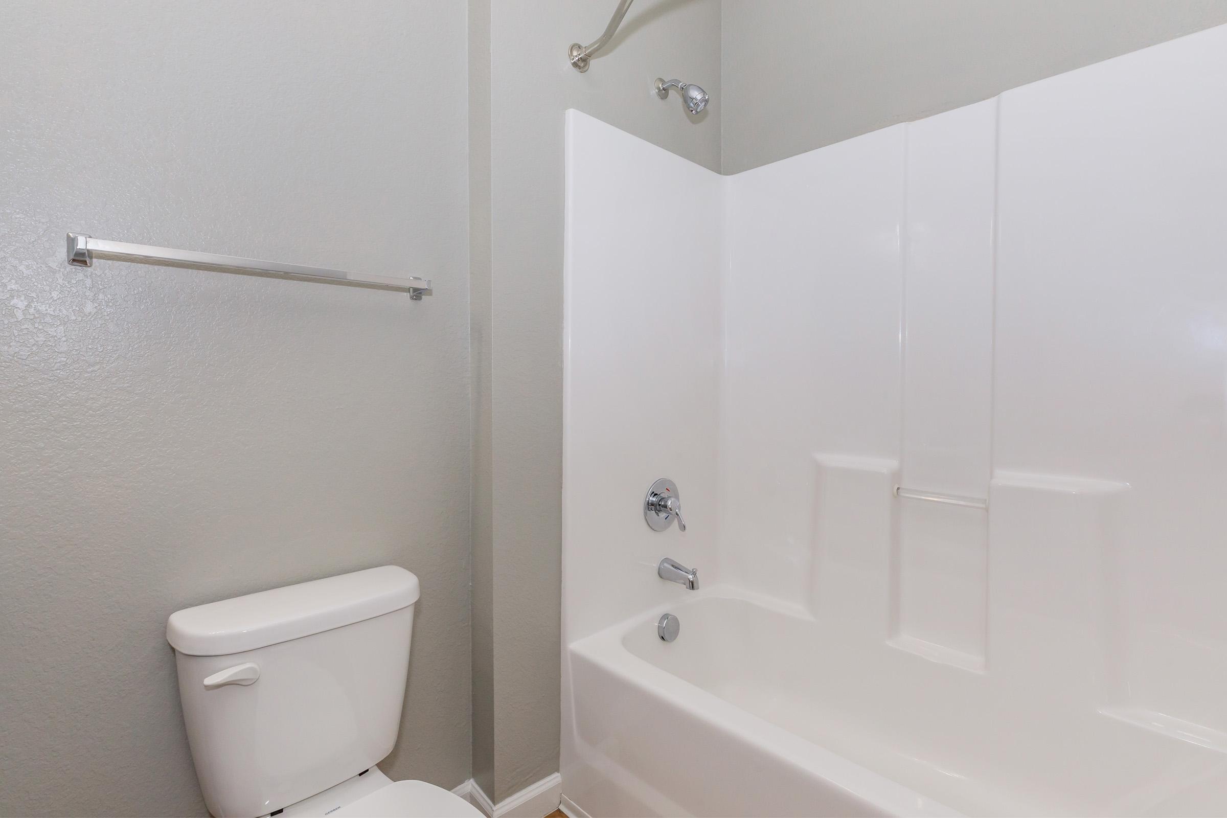 A clean, modern bathroom featuring a white bathtub and shower combination, a toilet, and a towel bar. The walls are painted in a light gray color, creating a bright and spacious atmosphere. The fixtures have a sleek design, ideal for a contemporary home environment.