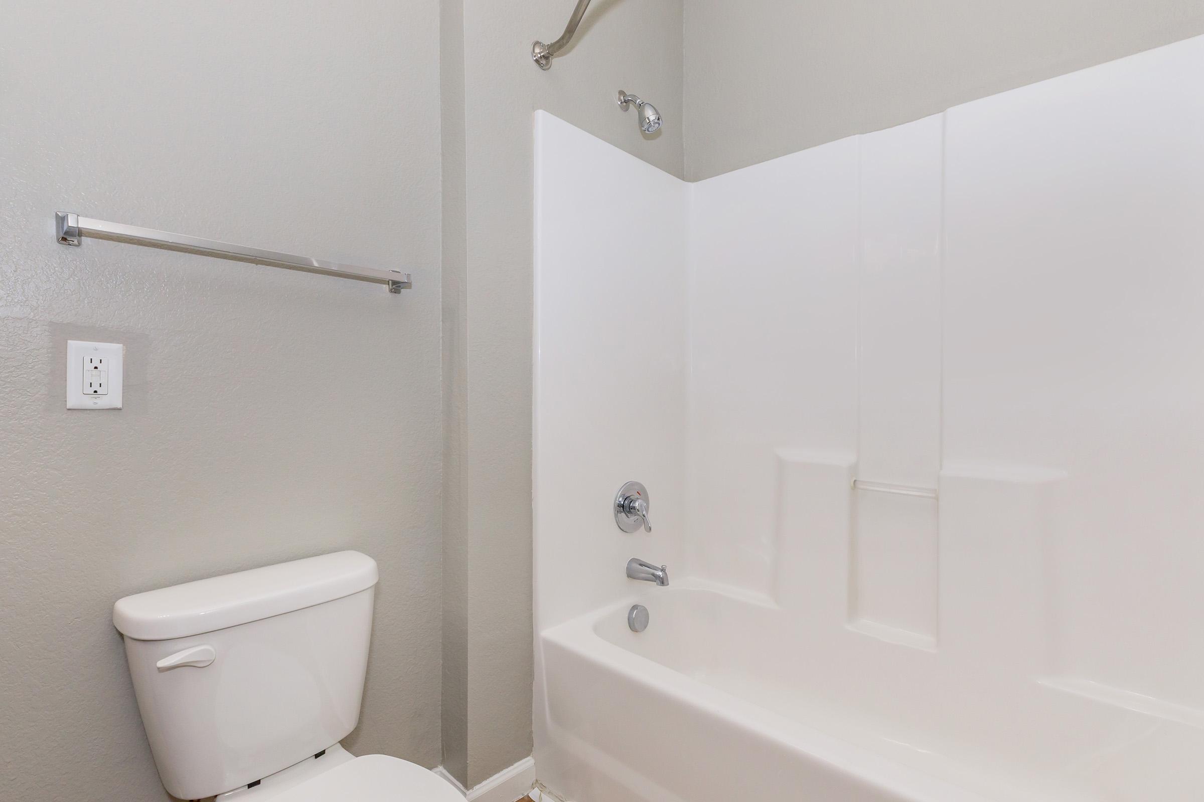 A clean, modern bathroom featuring a white tub with a shower, a toilet, and light gray walls. The space is uncluttered with basic fixtures, giving it a simple and functional appearance.