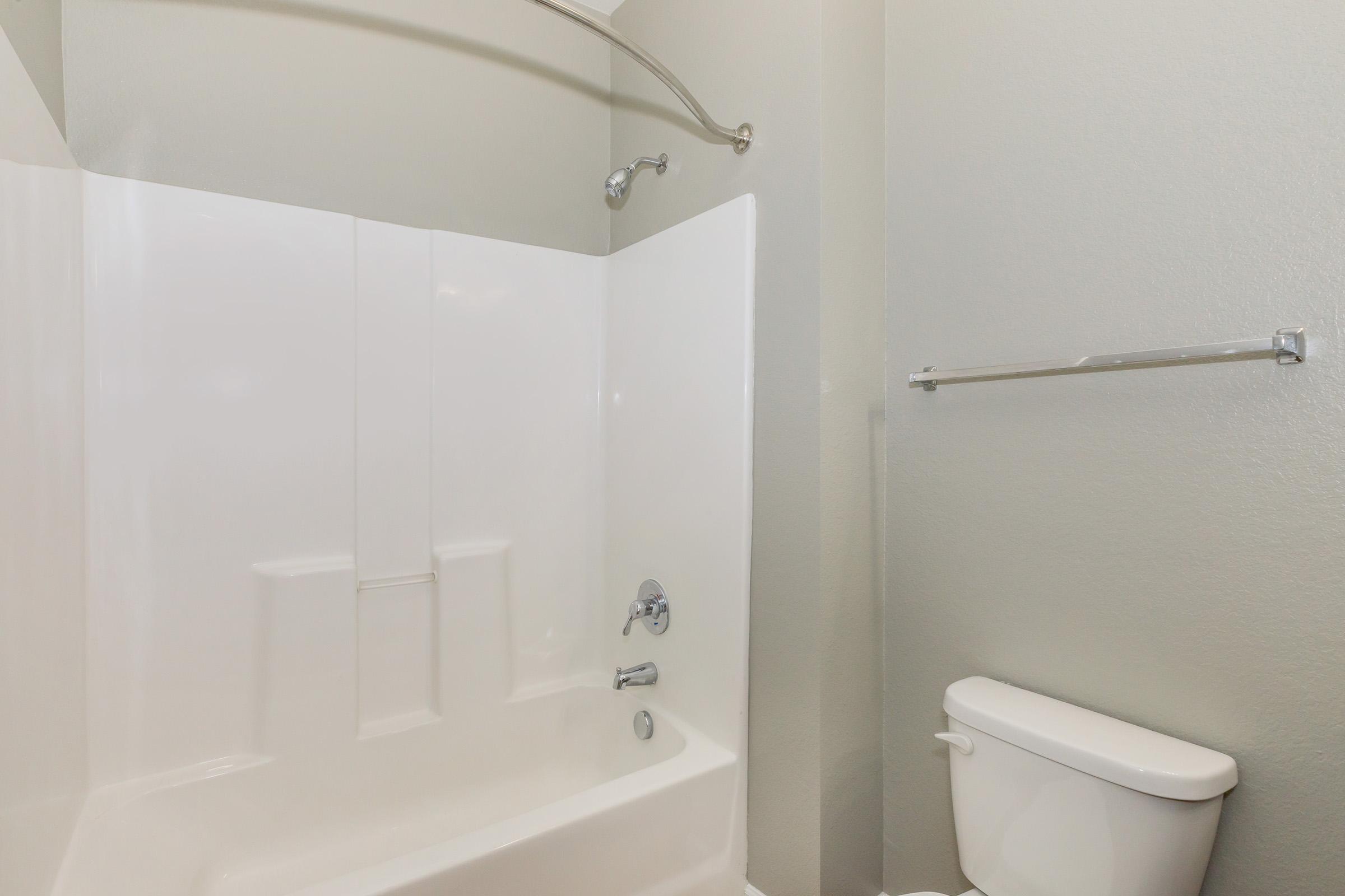 A clean, modern bathroom featuring a white bathtub with a showerhead and a chrome grab bar. There's a white toilet beside the bathtub, and the walls are painted a light green color, creating a fresh and bright atmosphere.